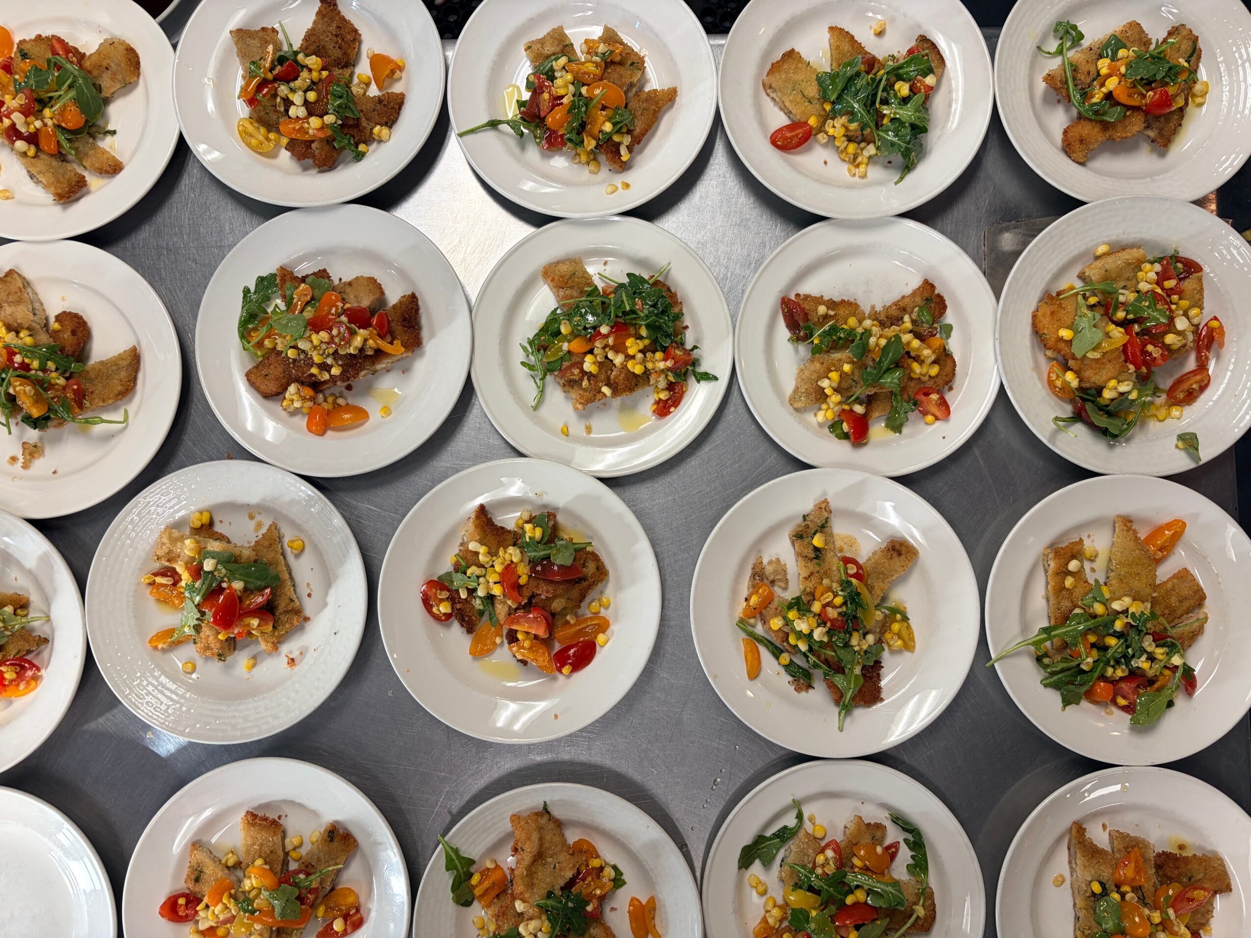 Multiple small white plates with colorful food arranged in a grid pattern on a gray surface.