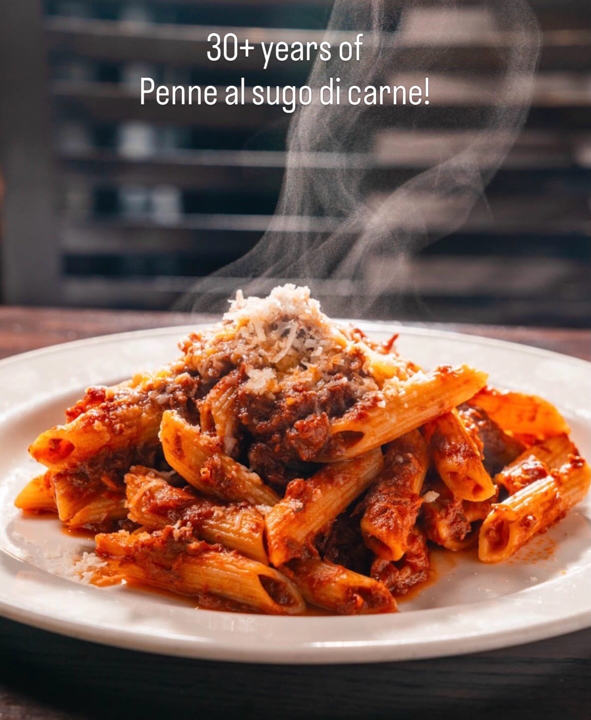 Plate of steaming penne pasta with meat sauce, with steam rising, on a white plate against a dark background.