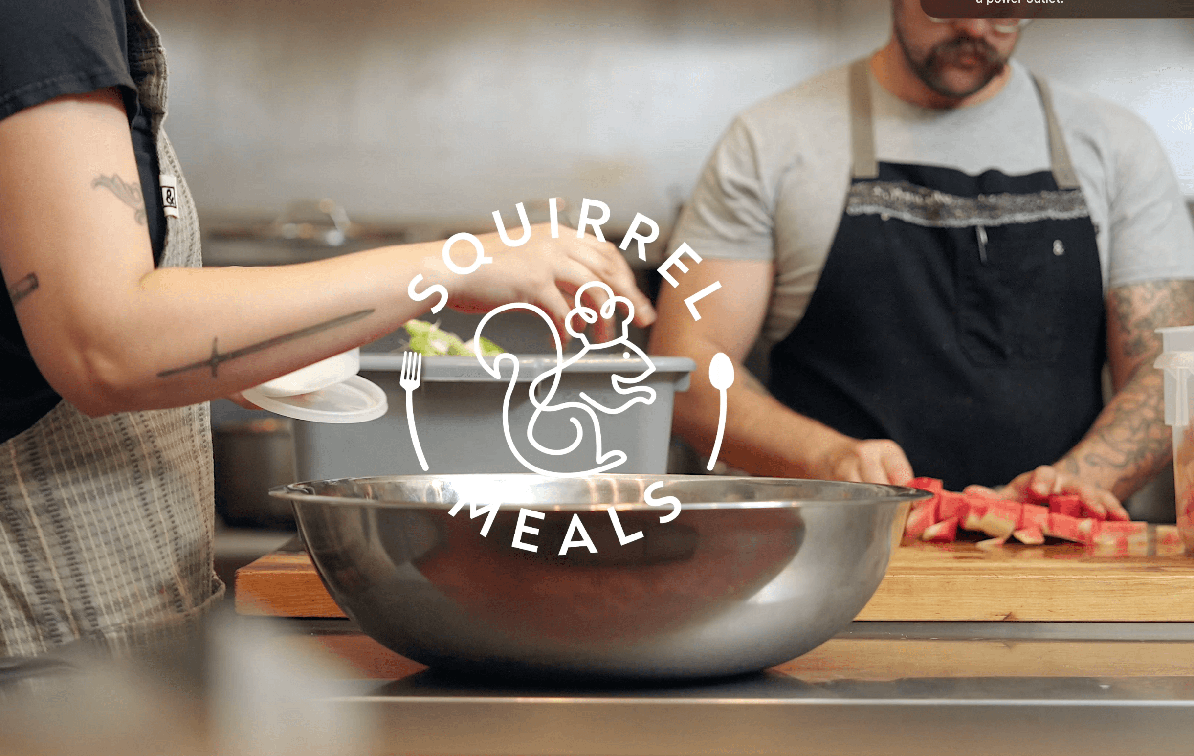 Two people prepare food in a kitchen, one holding a spoon over a large metal bowl, the other chopping ingredients on a cutting board, logo overlay