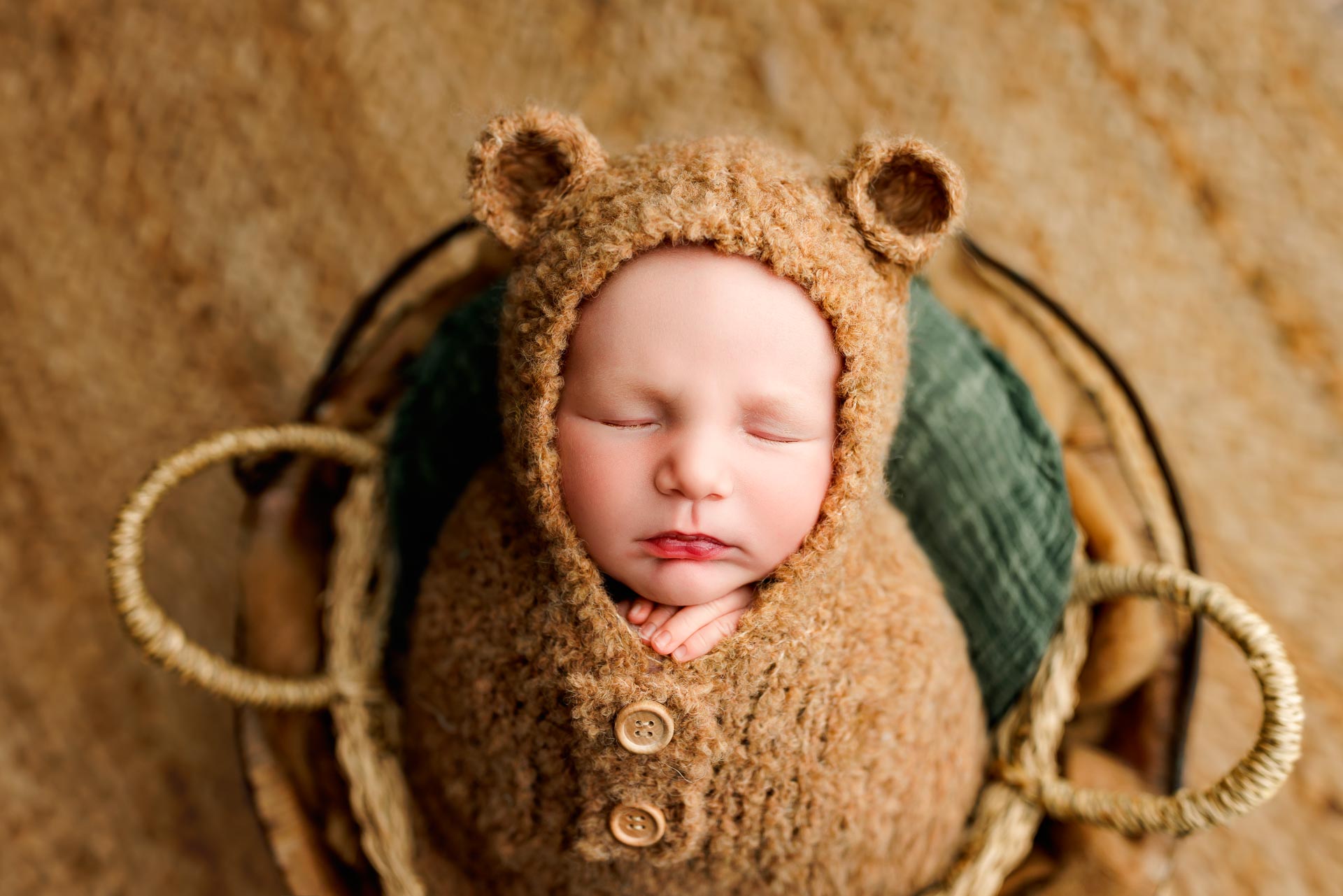 Baby wearing a bear hat with ears, wrapped in a cozy outfit, lying on a blanket, eyes closed, peaceful expression.