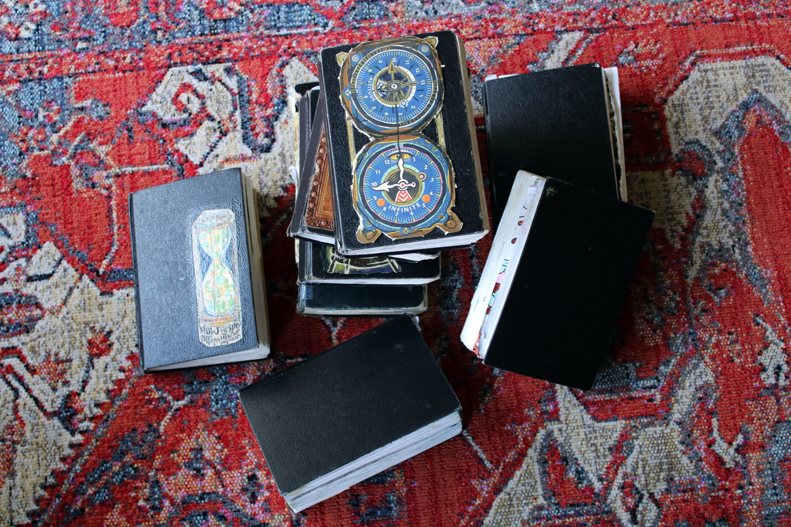Stack of black and colorful boxes and cards on a red patterned rug, some with circular designs, some with rectangular shapes.