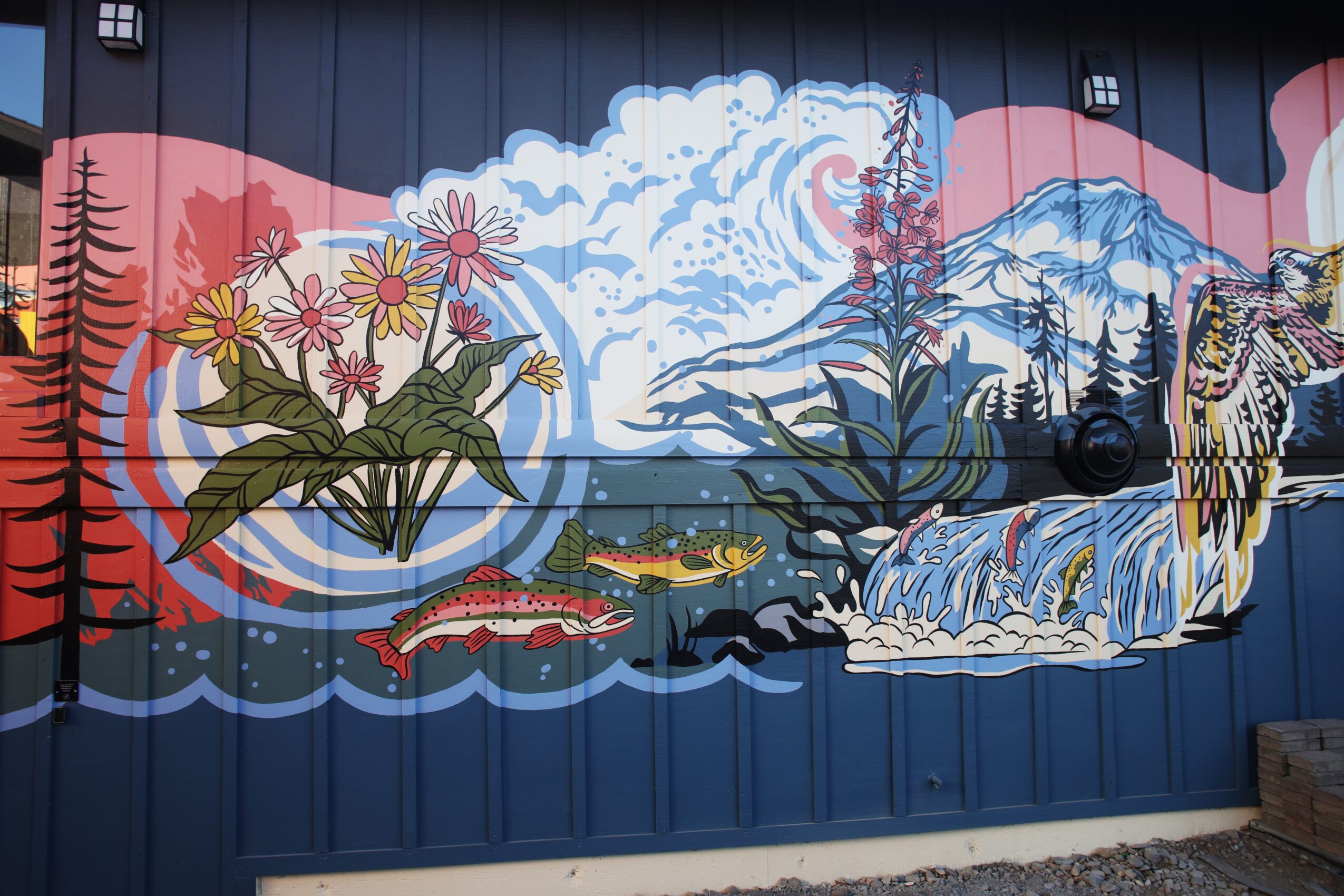 Colorful mural depicting flowers, a waterfall, fish, and mountains with clouds, painted on a blue wall.