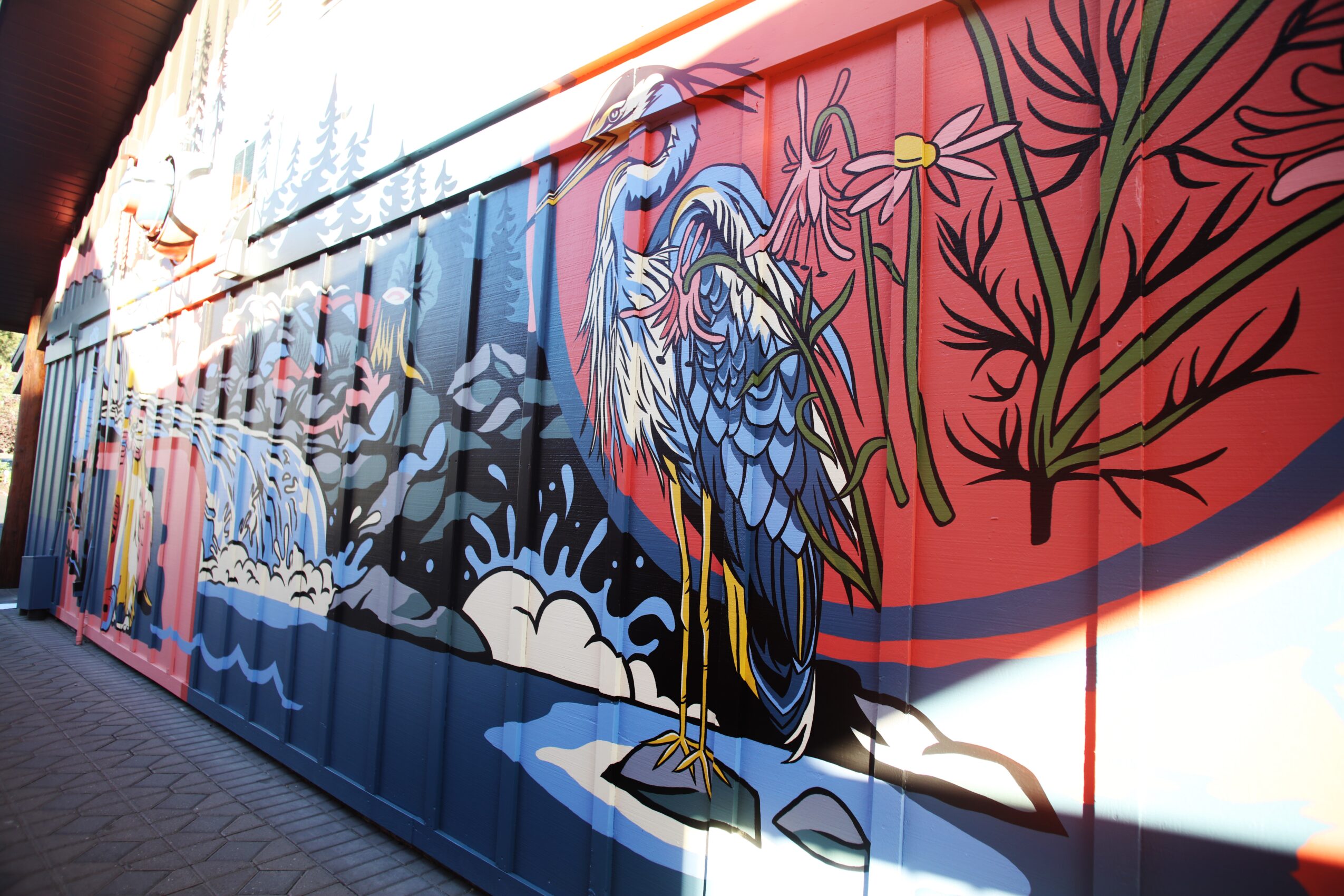 Colorful mural featuring a heron standing on rocks near water with plants and flowers in the background.