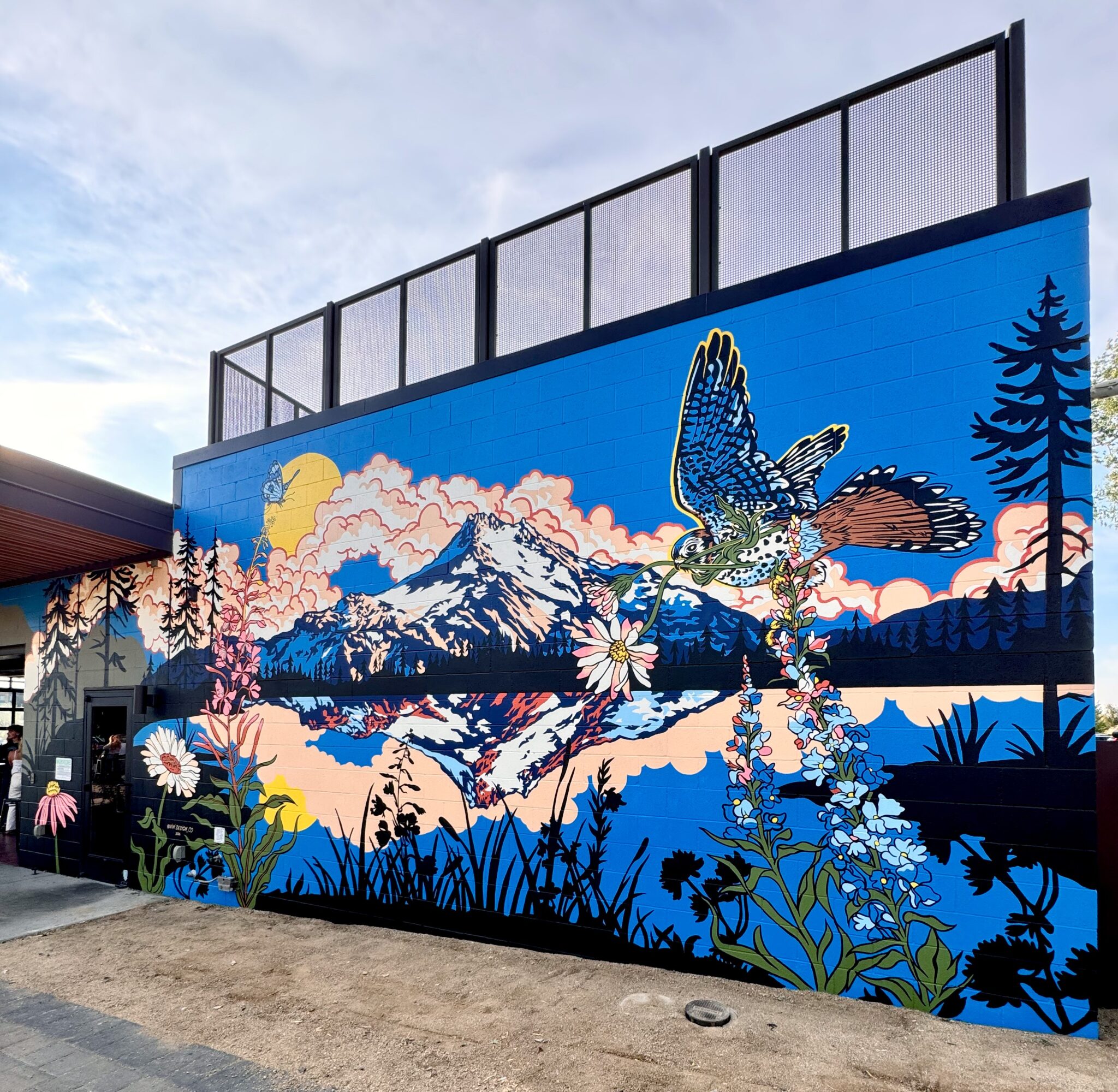 Colorful mural of mountains, a bird, flowers, and trees against a blue sky background.