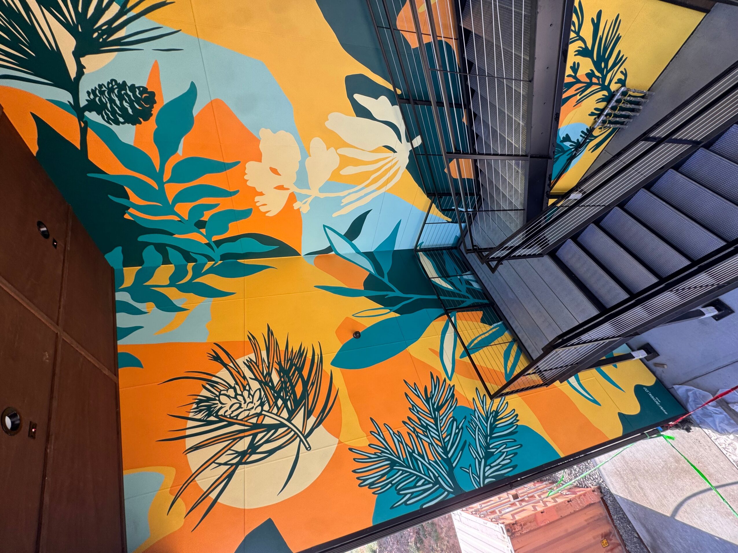 Colorful wall with large floral and leaf patterns in blue, white, orange, and yellow, next to an escalator.