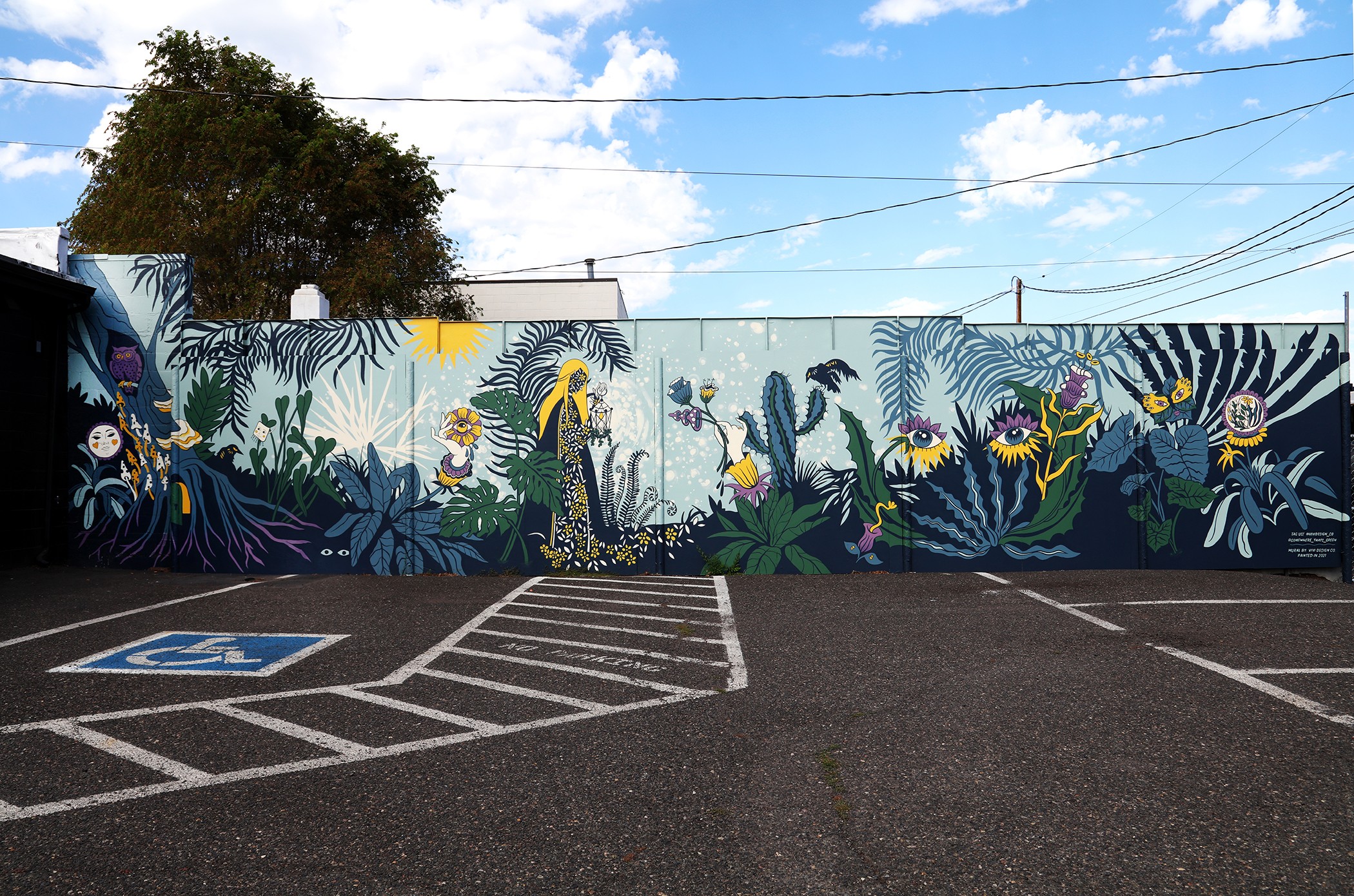 Colorful mural of plants and flowers on a wall, with a parking lot and a handicapped space in foreground.