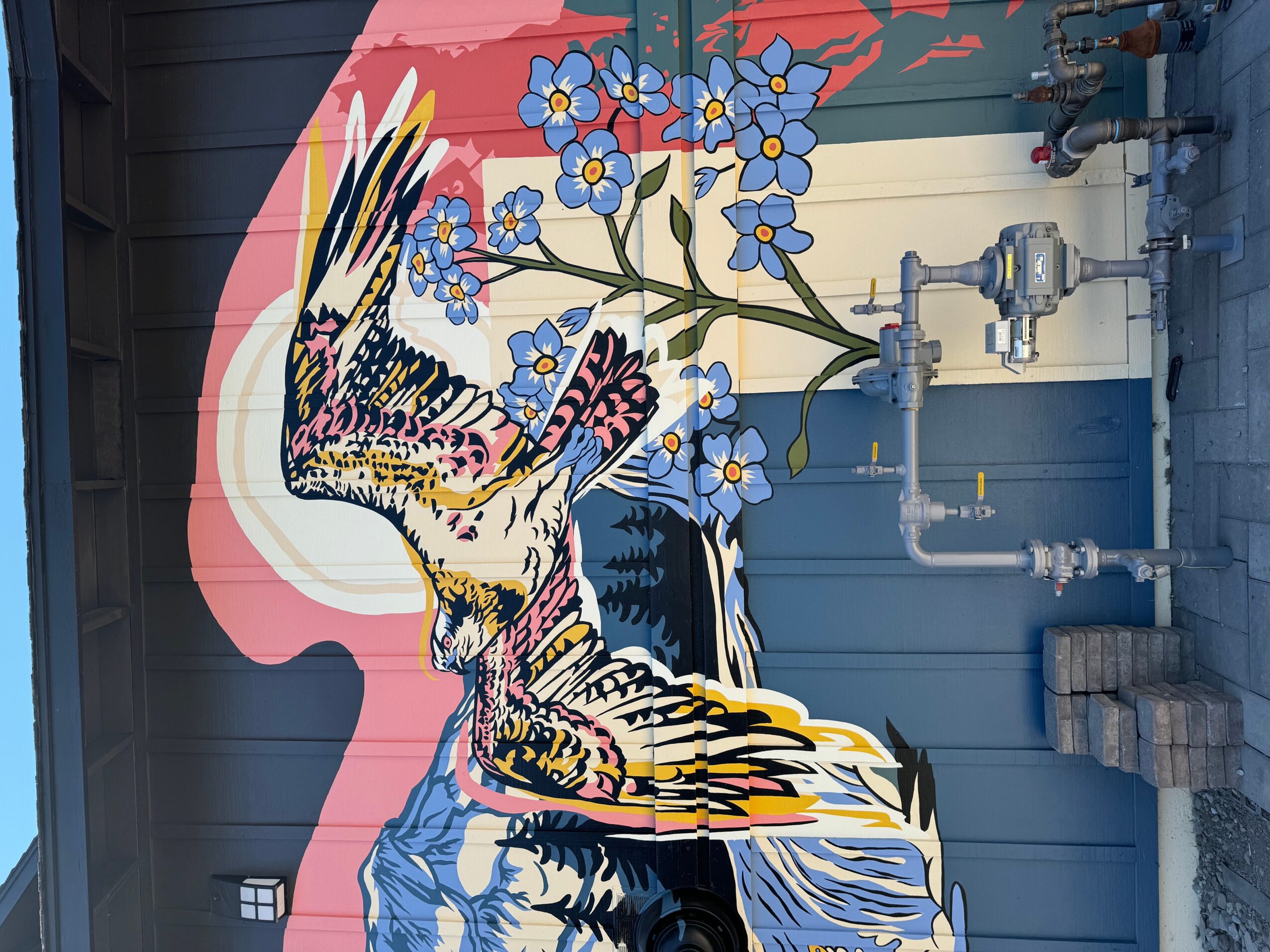 Wall mural of a bird perched on blue flowers with pipes and a blue wall background.