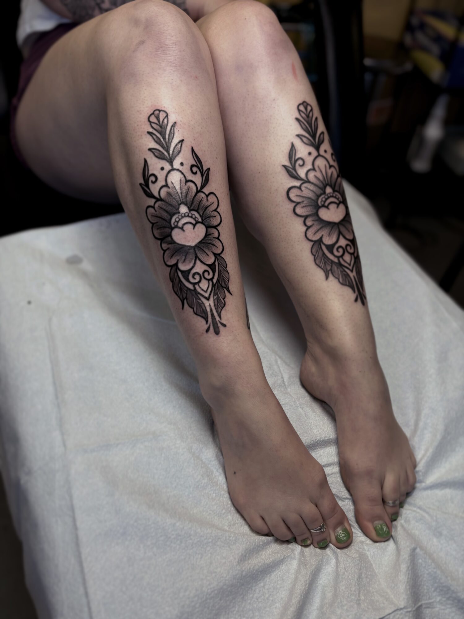 Person's legs with floral tattoos on calves, resting on a white surface, background blurred.