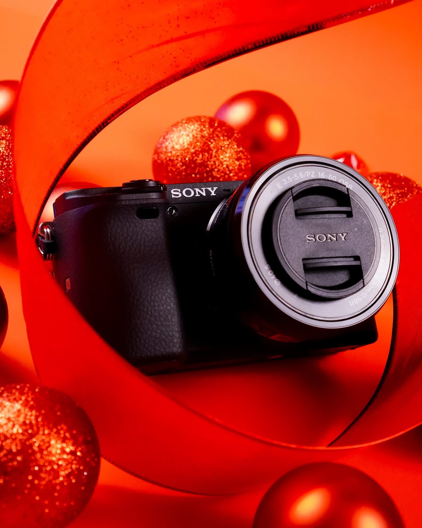 Camera with a lens cap on, surrounded by red and gold Christmas ornaments and decorations.