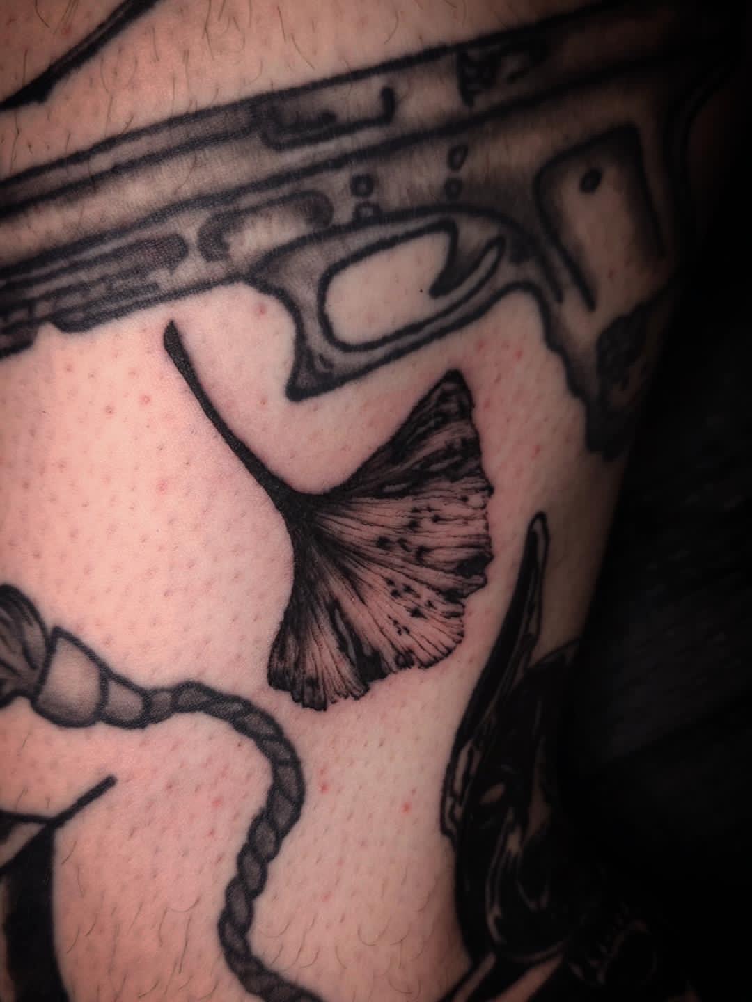 Close-up of a tattoo featuring a butterfly and part of a gun, with detailed line work and shading.