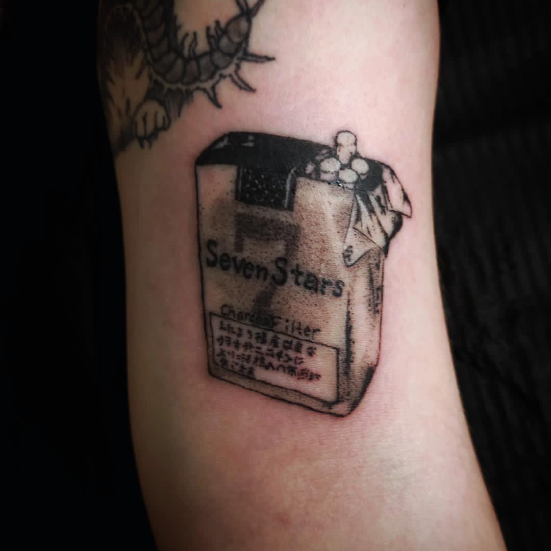 Tattoo of a lighter with text and symbols, including 'Seven Stars' and other characters, on a person's arm.