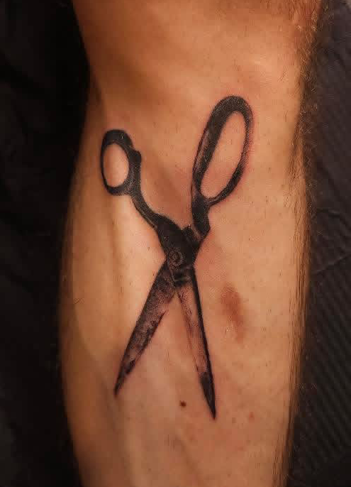 Tattoo of scissors on person's arm, with blades open and handles pointing upward.