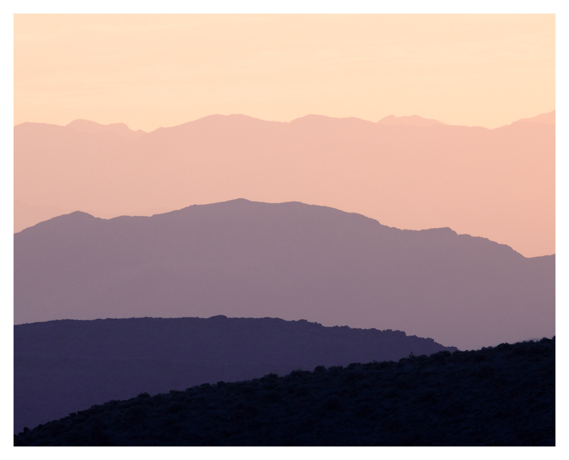 Layered mountain silhouettes against a pastel sky, viewed from below, with soft colors and varying heights.