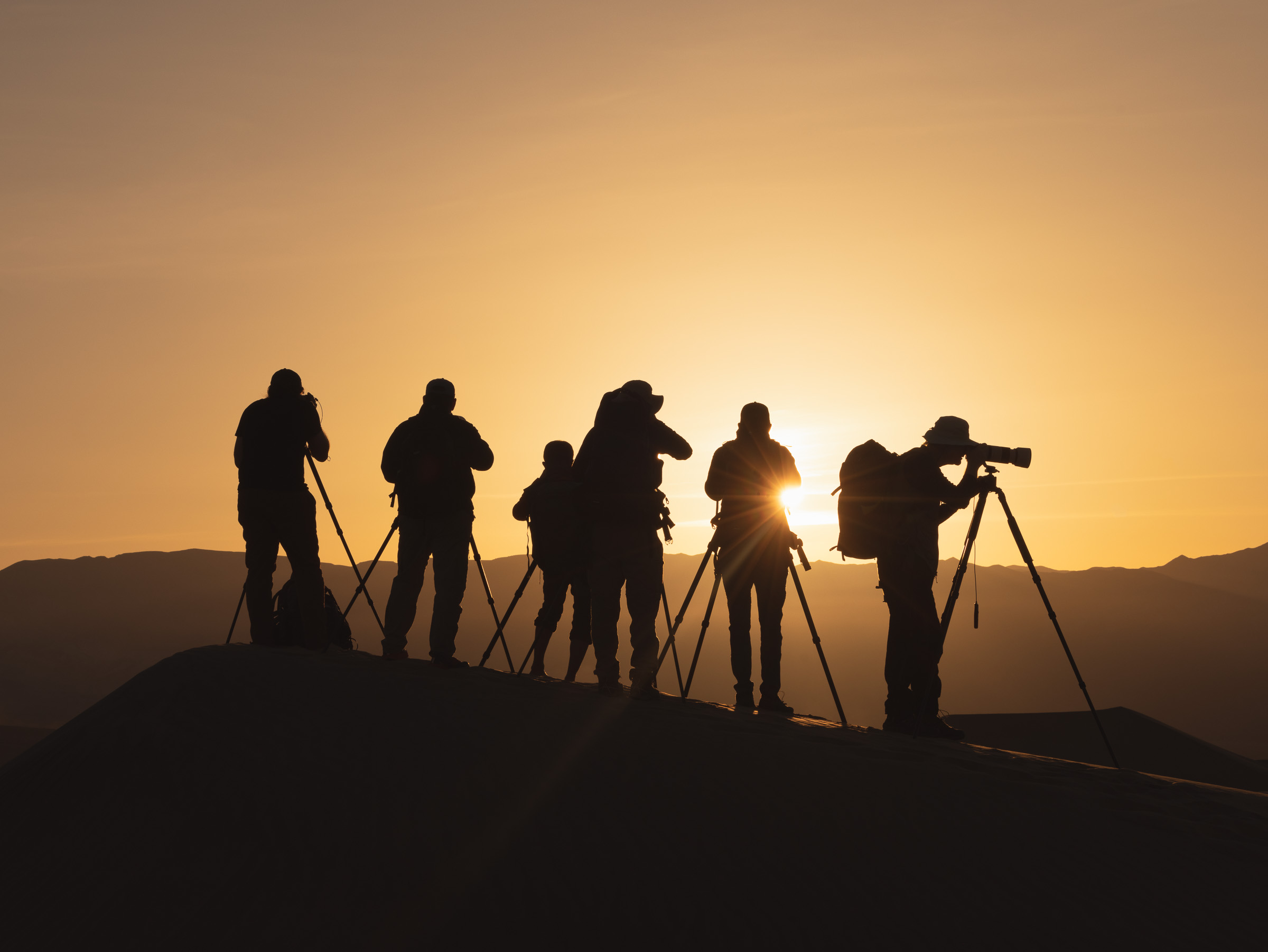 Silhouettes of five photographers with tripods against a sunset sky, standing on a hilltop.