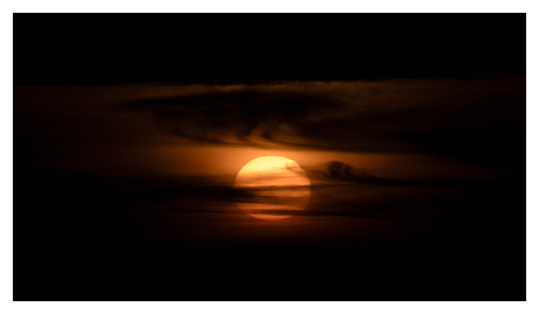 Sunset with a partially obscured sun and dark clouds, creating a dramatic sky.