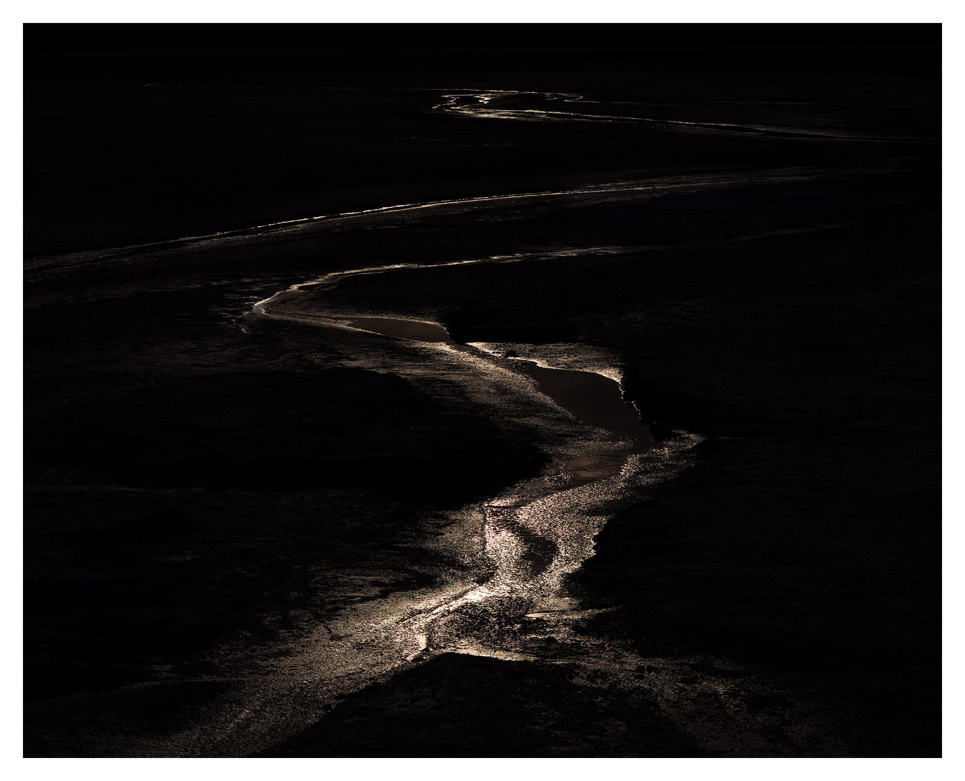 Dark landscape with a winding, illuminated river or stream, minimal light, and a mostly black background.