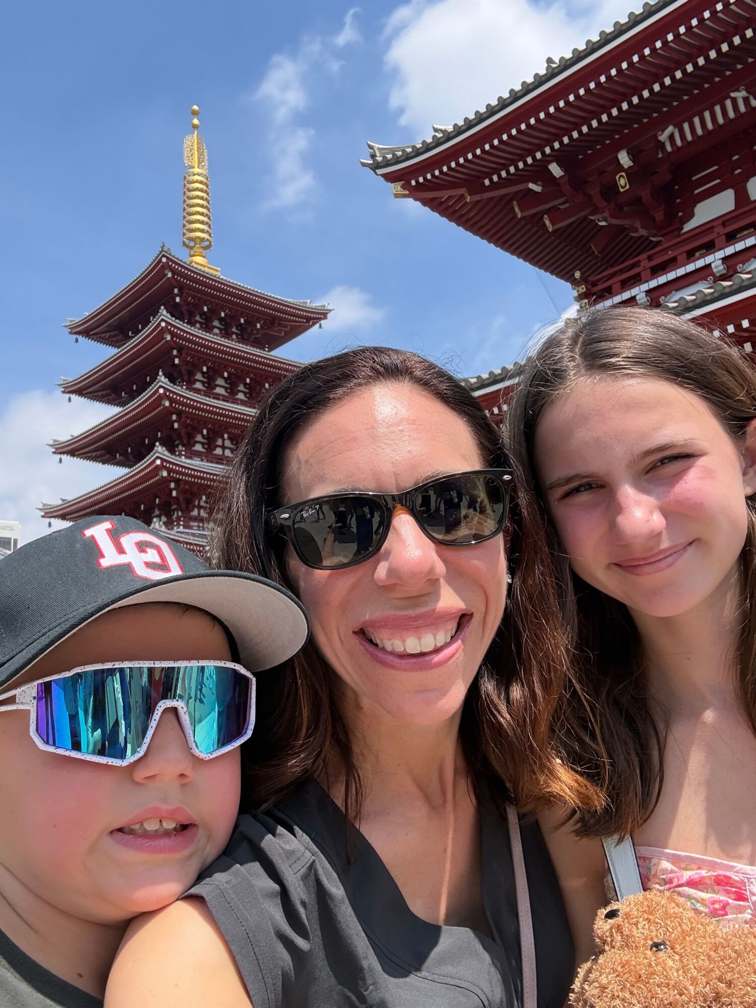 Three people smiling outdoors with a traditional Asian pagoda-style building in the background.
