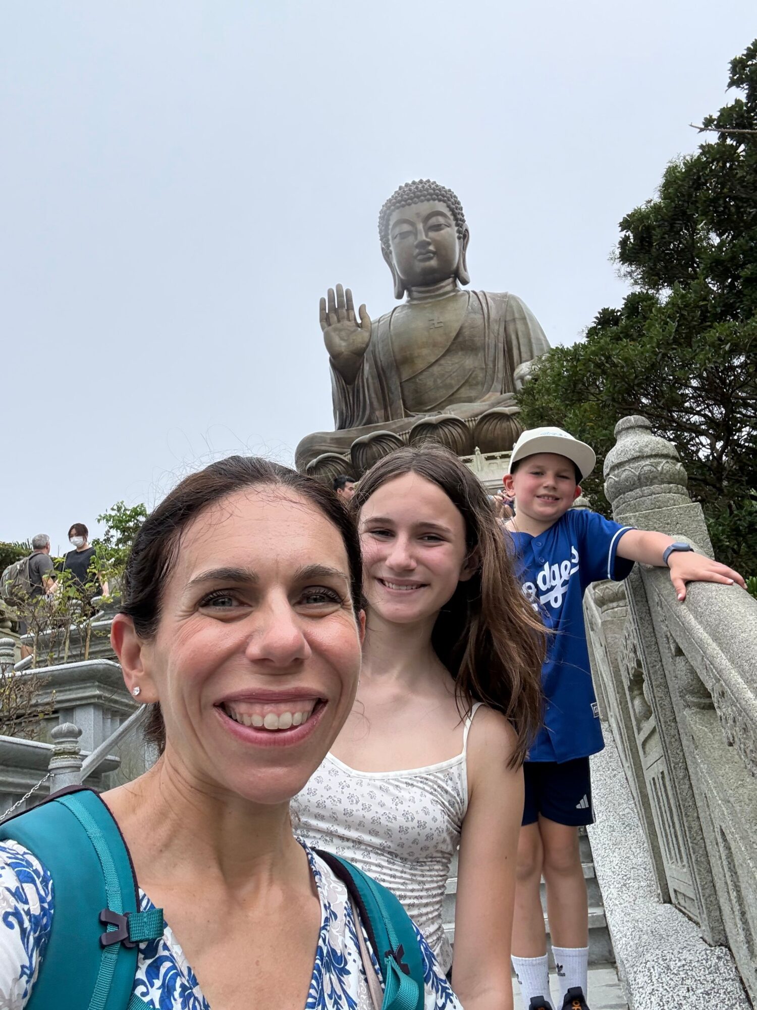 Two women and a child taking a selfie in front of a statue of a seated figure outdoors.