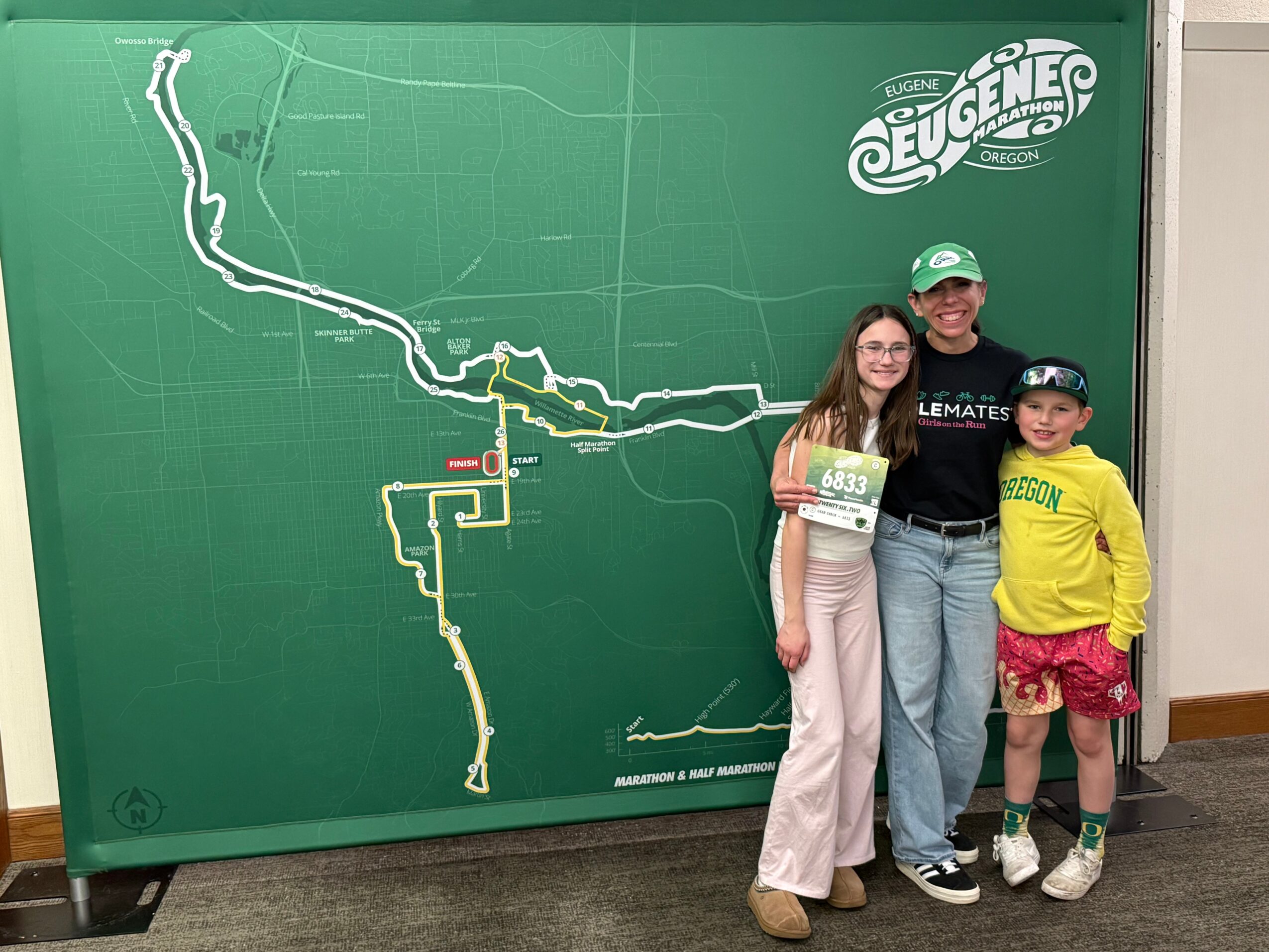 Three people stand in front of a large green map with a white logo, smiling and posing for a photo.
