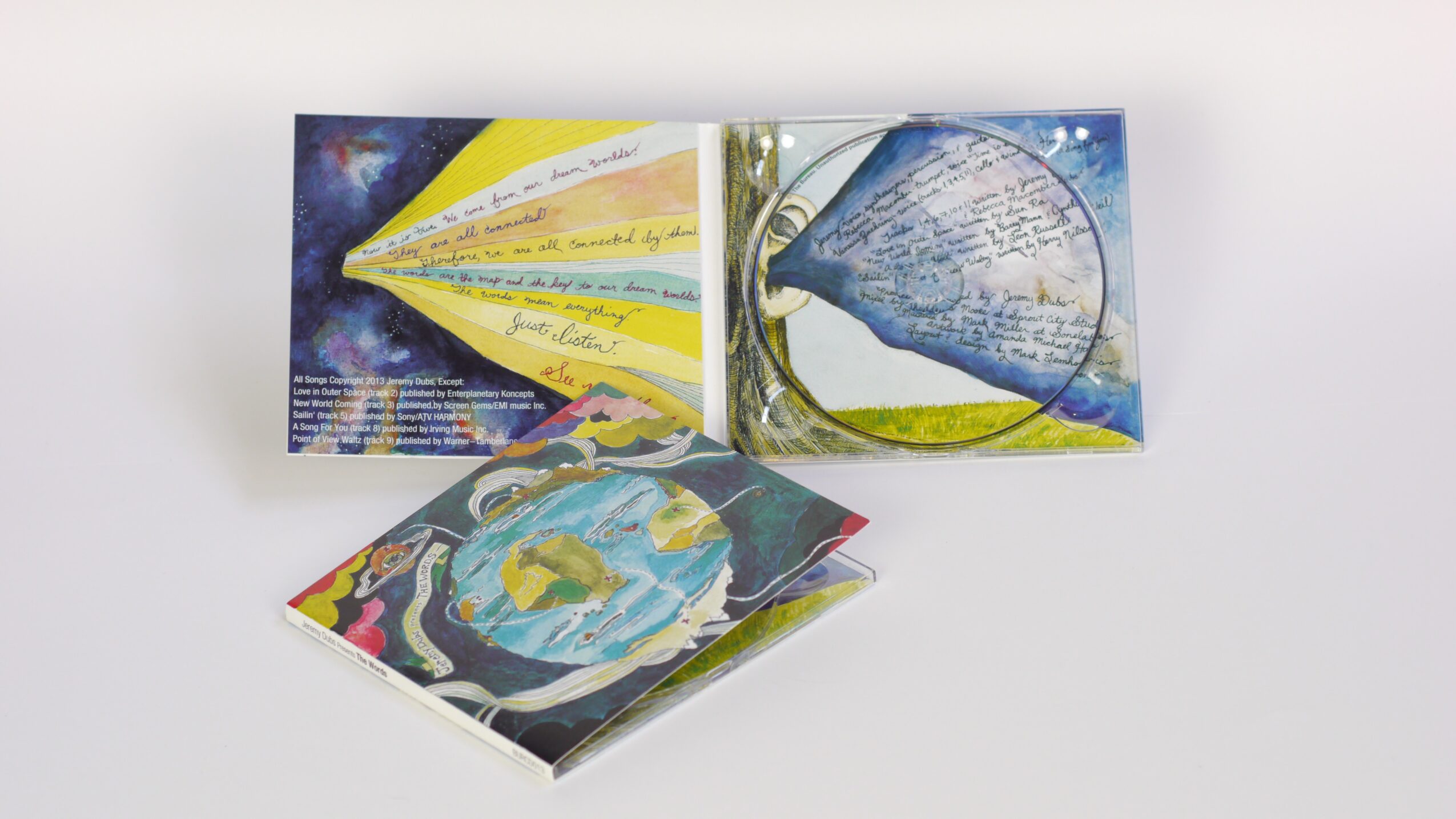 Three open books with colorful illustrations and handwritten text, displayed against a white background.