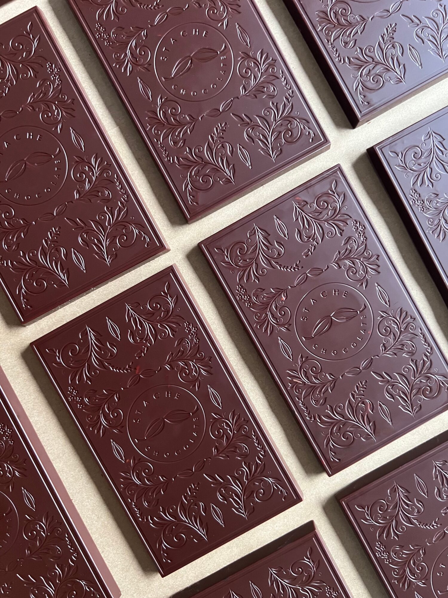 Multiple dark chocolate bars with embossed floral and decorative patterns, arranged diagonally on a white surface.