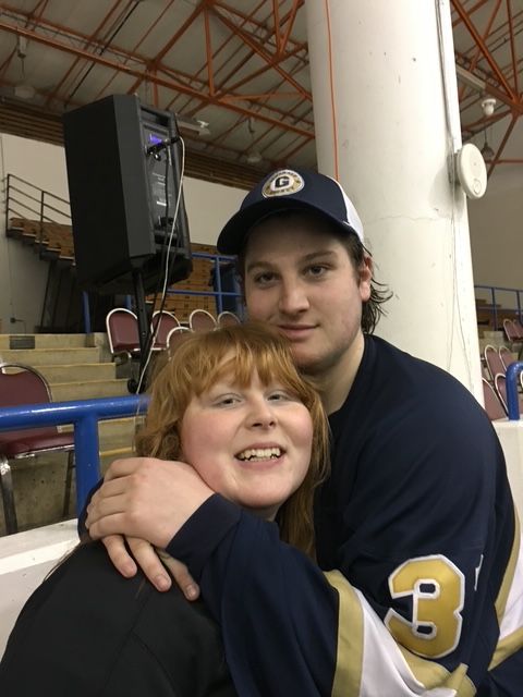 Two people, one with dark hair and a cap, and a child with red hair, smiling and hugging in a workshop.