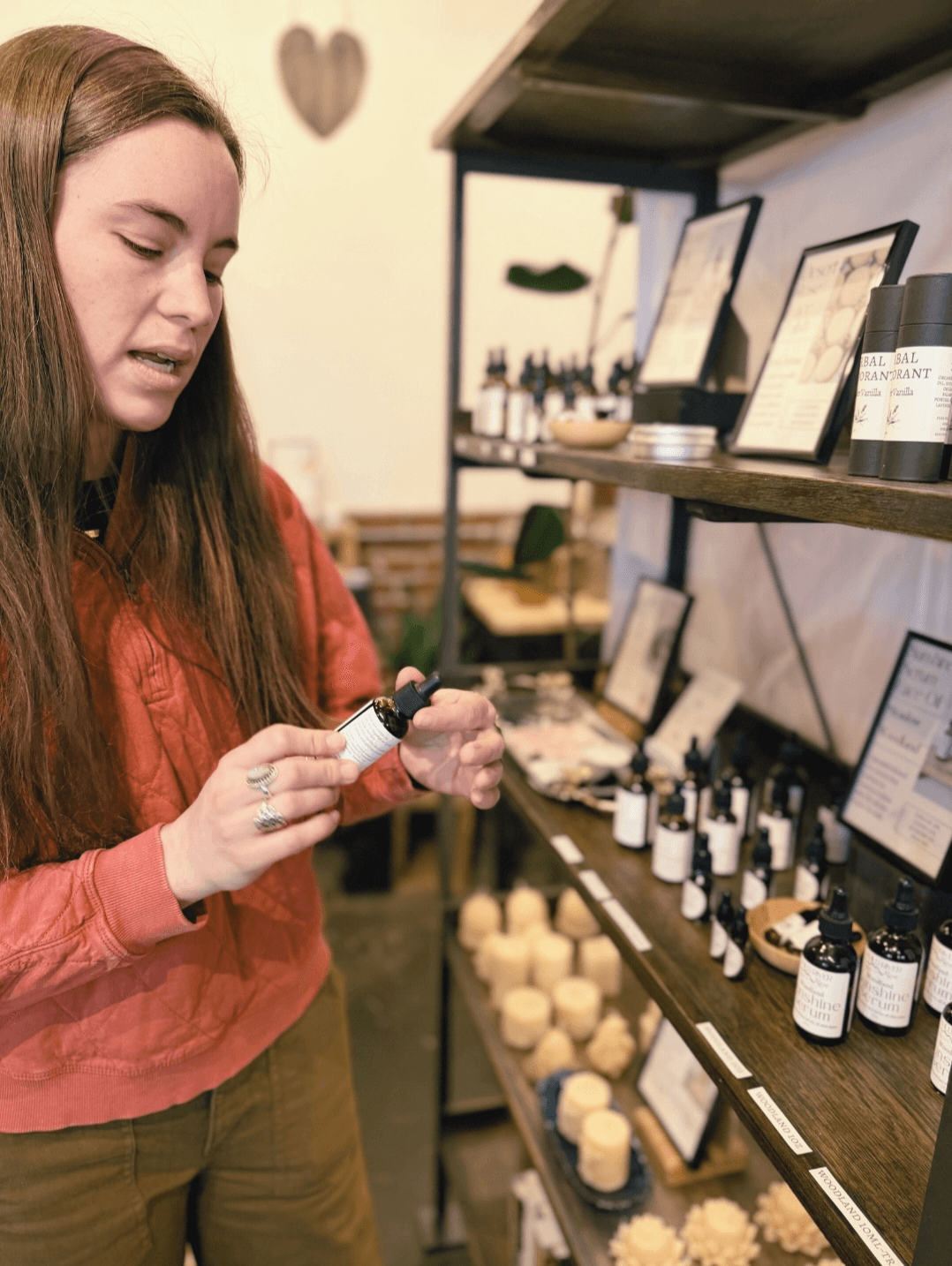 Young woman in a store examining a small bottle, shelves with various bottles and products behind her.