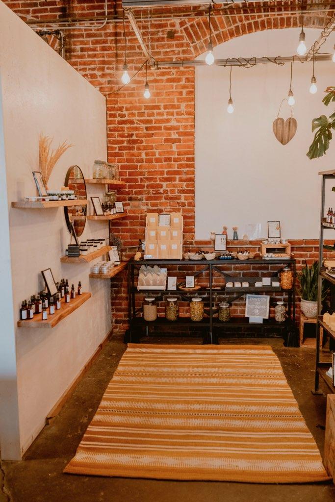 Interior of a store with brick and white walls, wooden shelves, and a striped rug on the floor.