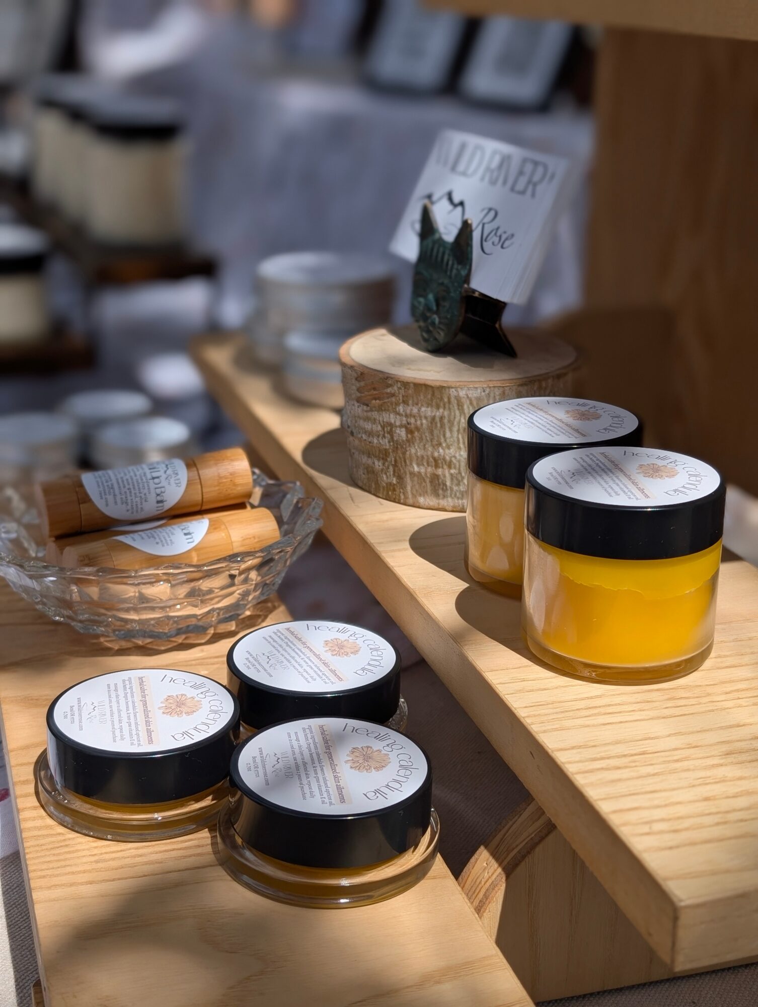 Display of yellow jars with black lids on a wooden shelf, with other containers and a sign in the background.