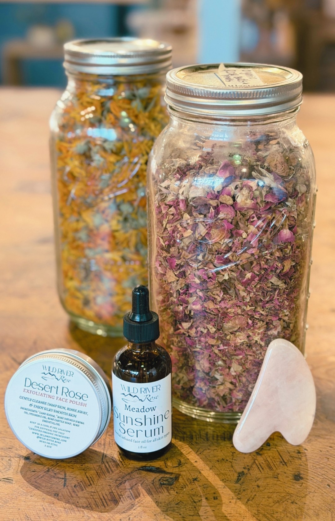 Two glass jars filled with dried flowers, a small container, a dropper bottle, and a white stone on a wooden surface.