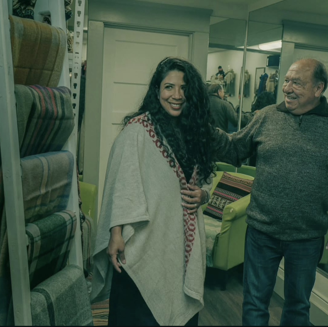 Woman with curly hair smiling, standing next to an older man in a store with fabric rolls and mirrors.