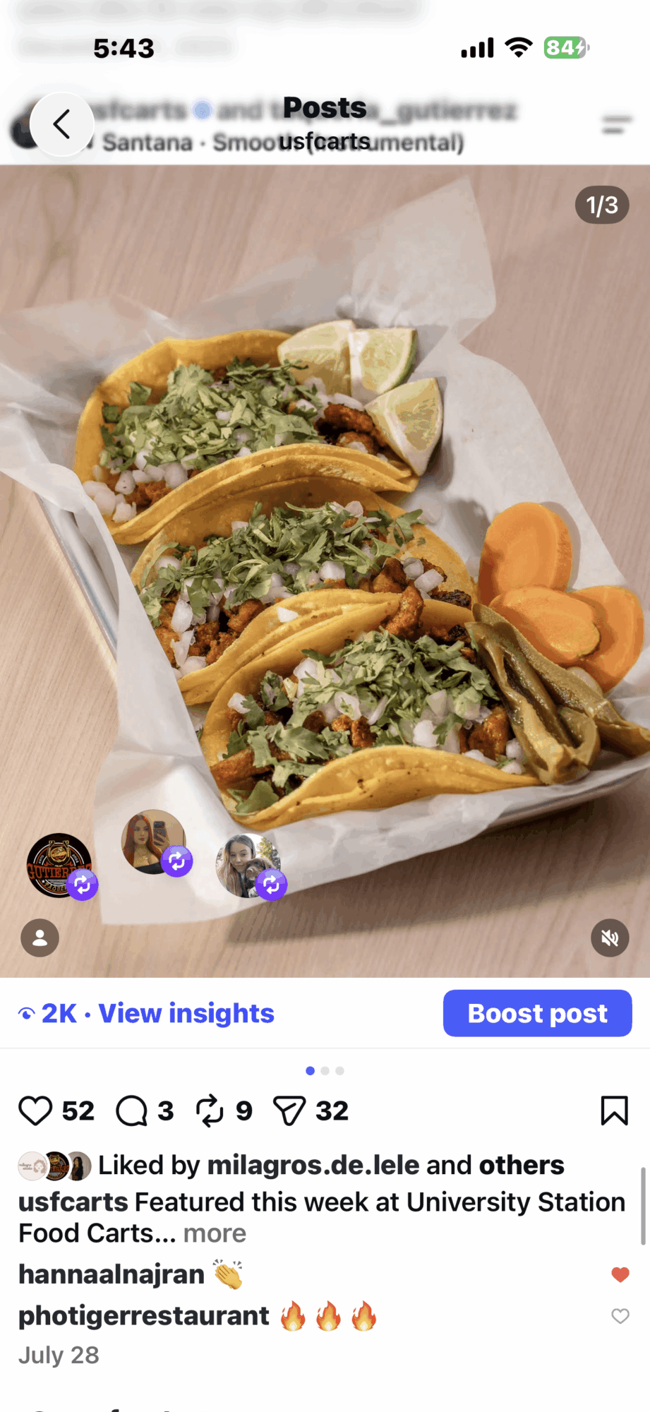 Three tacos with lettuce, meat, and cheese in a paper tray, with sliced carrots on the side, on a wooden surface.