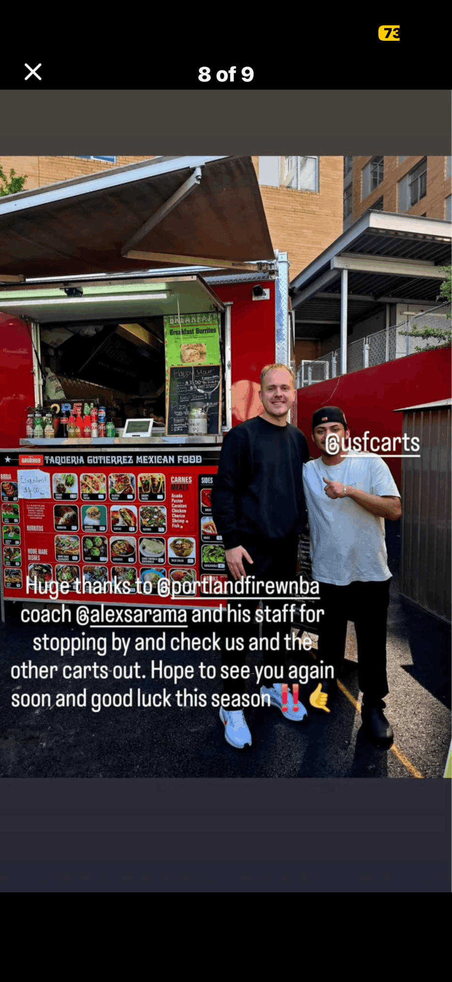 Two men standing in front of a red food truck with a menu, smiling outdoors. One man has a beard and is wearing a black jacket. Alt text word count: 20. Confidence: 0.9