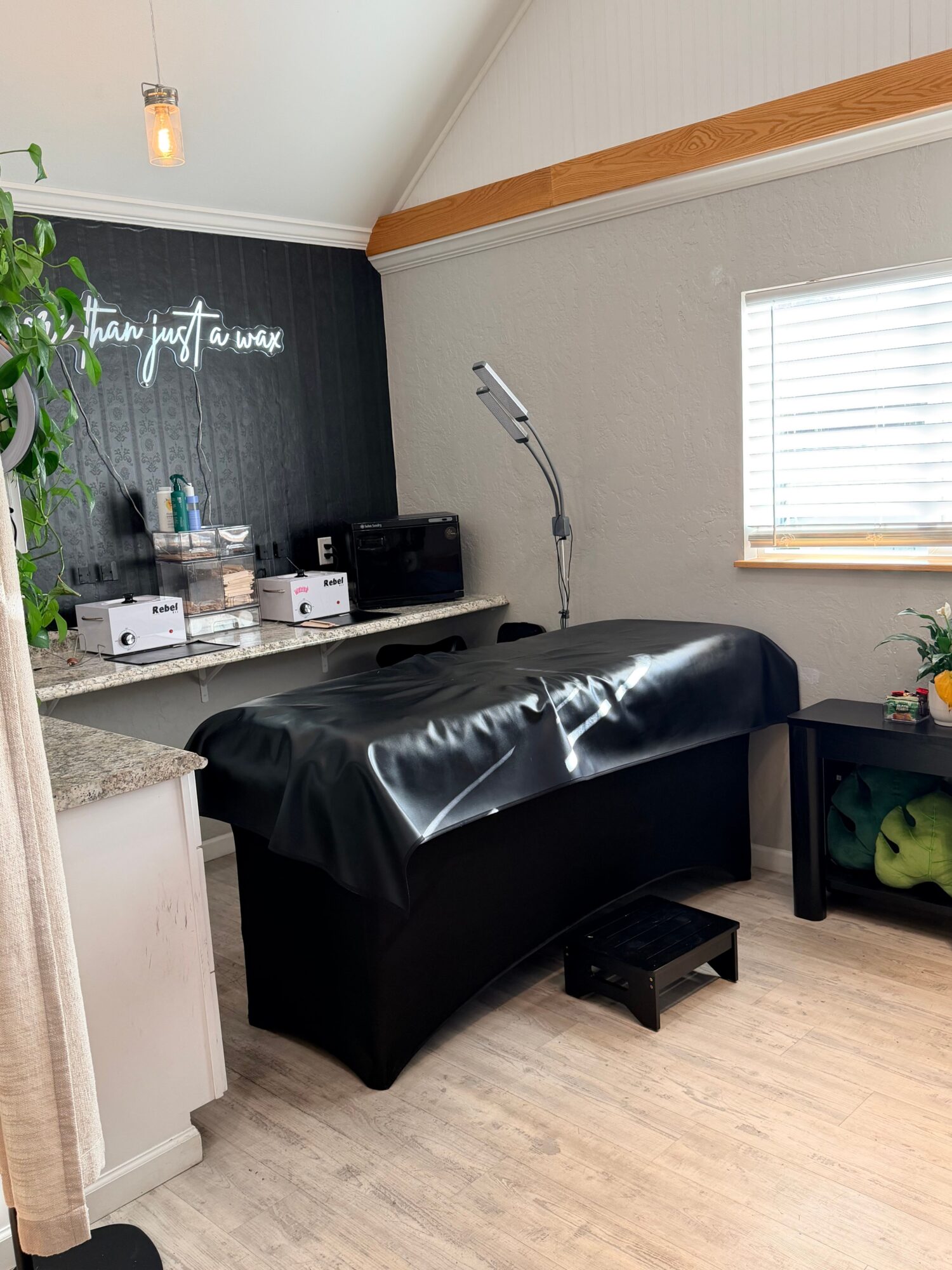 Living room with a black couch, a small table, and a window with blinds, hardwood floor, and a black wall with white text.