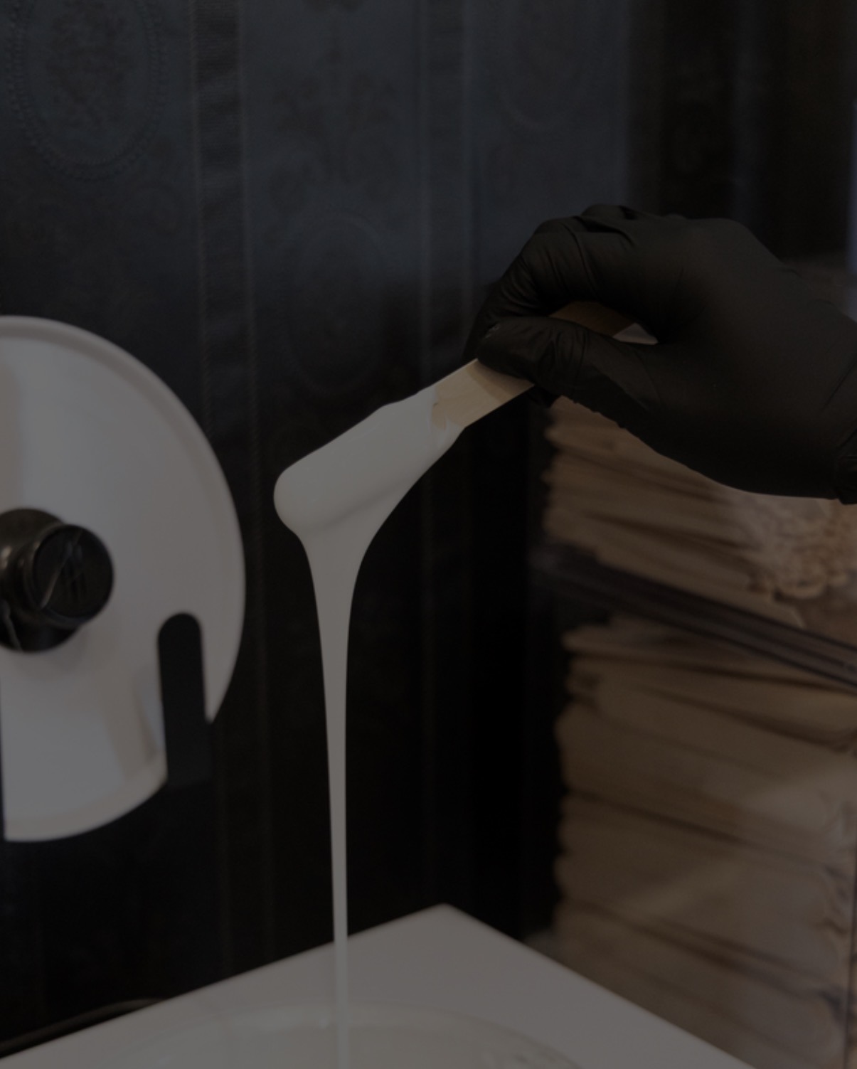 Person wearing black glove holding a white object with liquid pouring out, against a dark background, with a paper towel roll nearby.