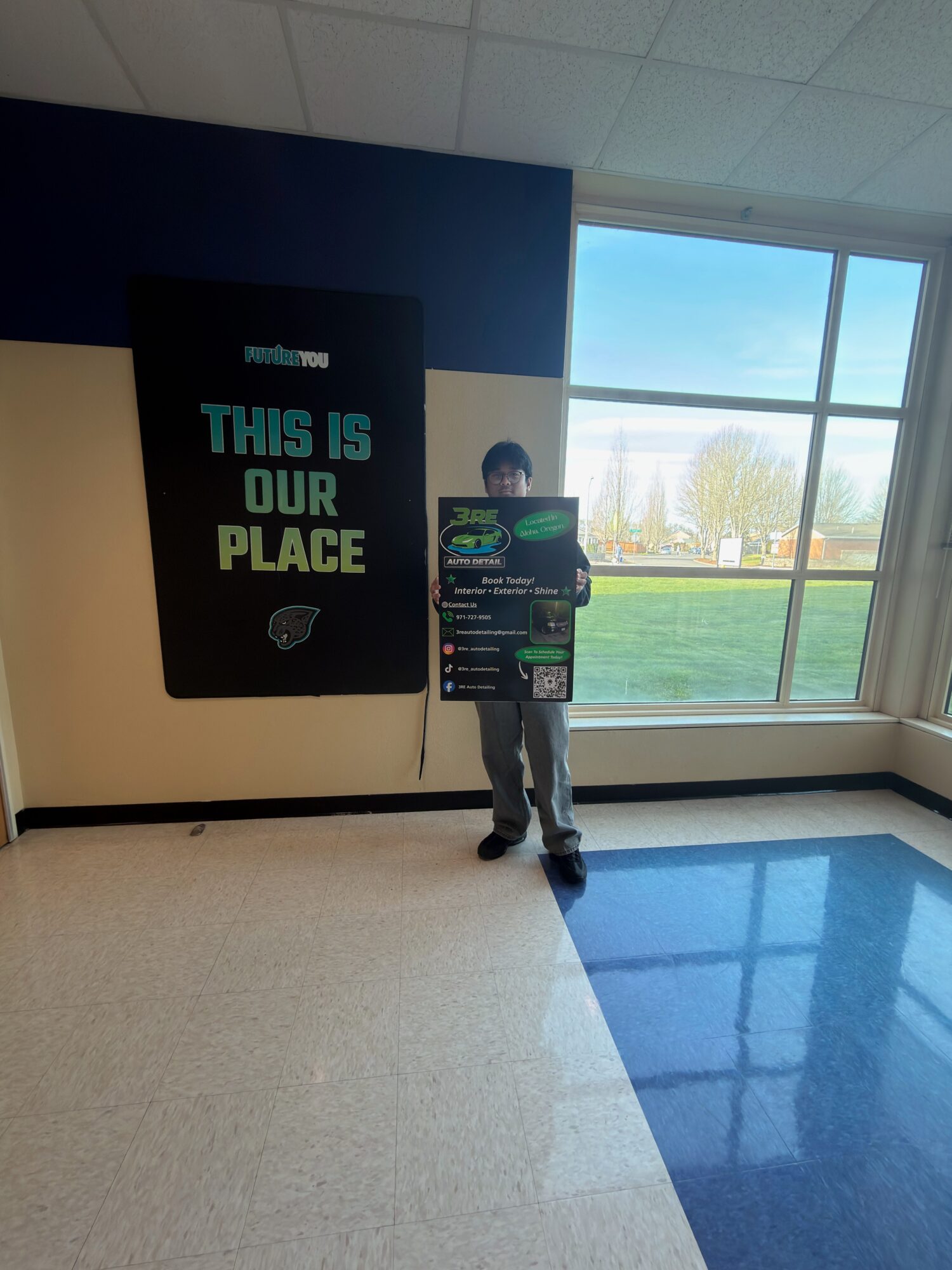 Child holding a large gaming poster in a brightly lit room with a large window showing outdoor scenery.