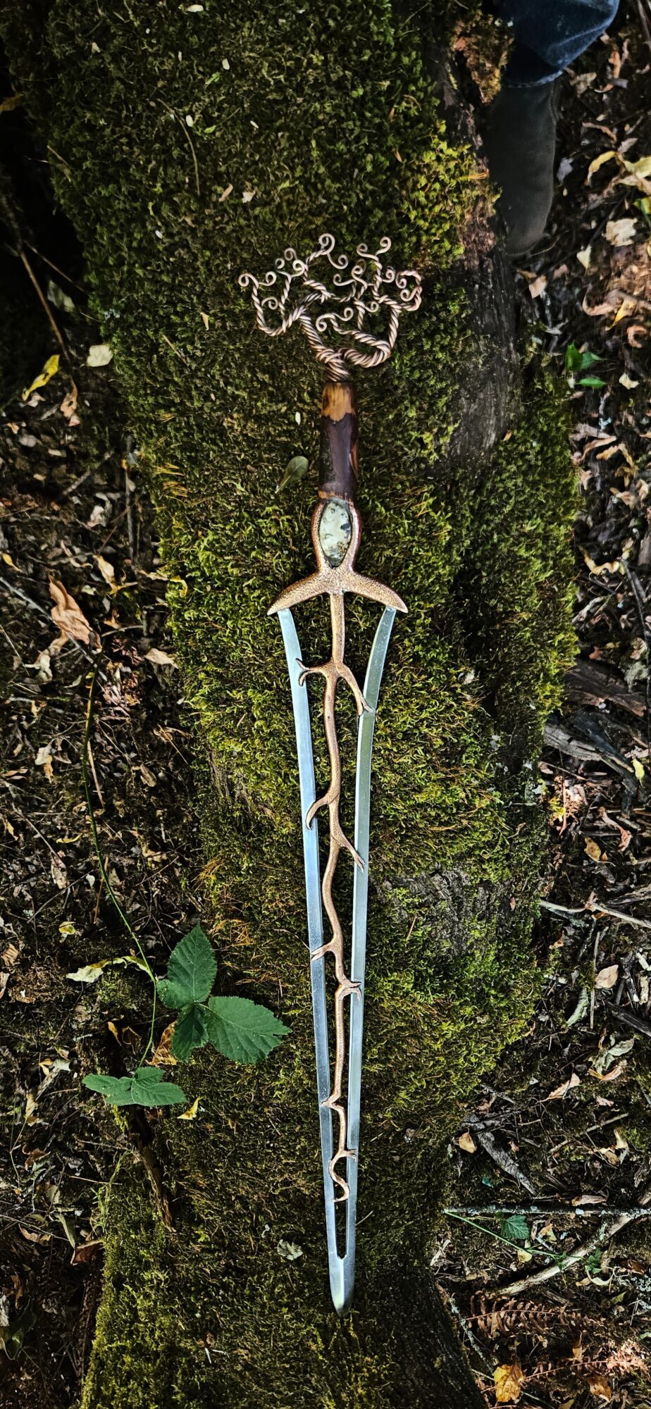 A metallic hairpin with decorative elements lies on mossy ground among leaves and small plants.