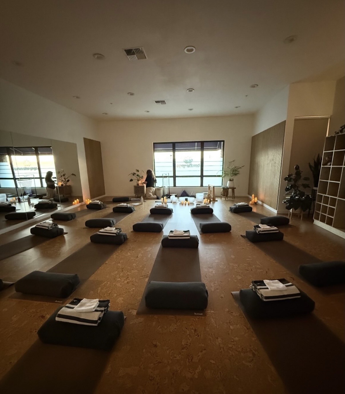 Yoga or meditation room with mats and cushions arranged on a wooden floor, large windows, and minimal decor.