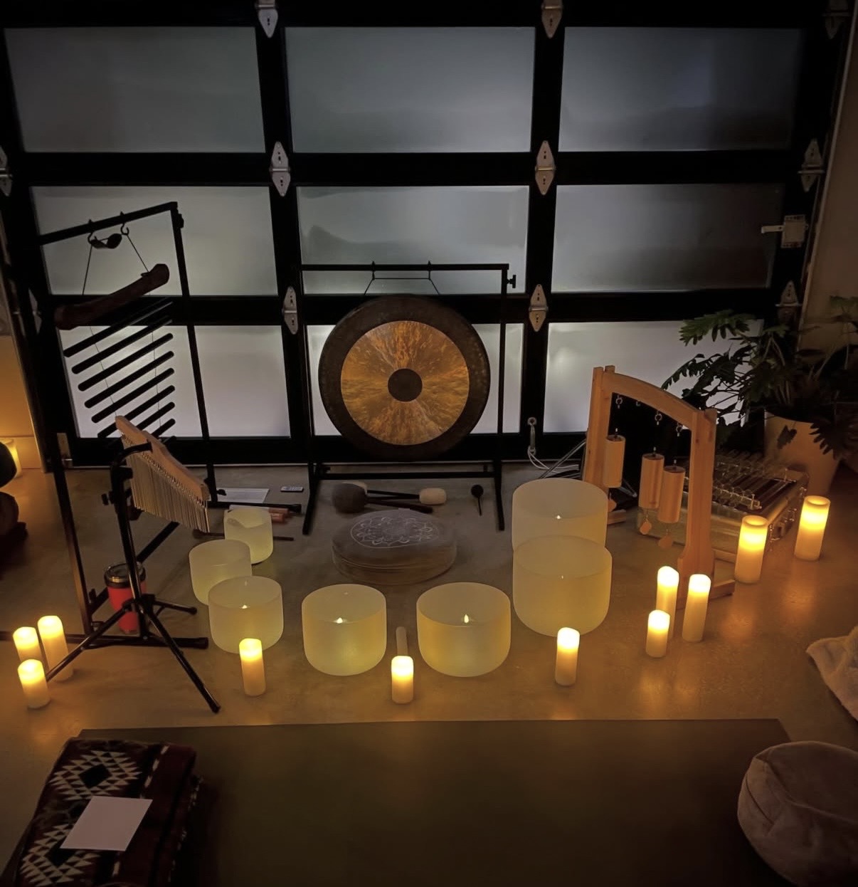 Indoor space with candles, musical instruments, and a large gong, viewed from above, with a dark ceiling and window panels.