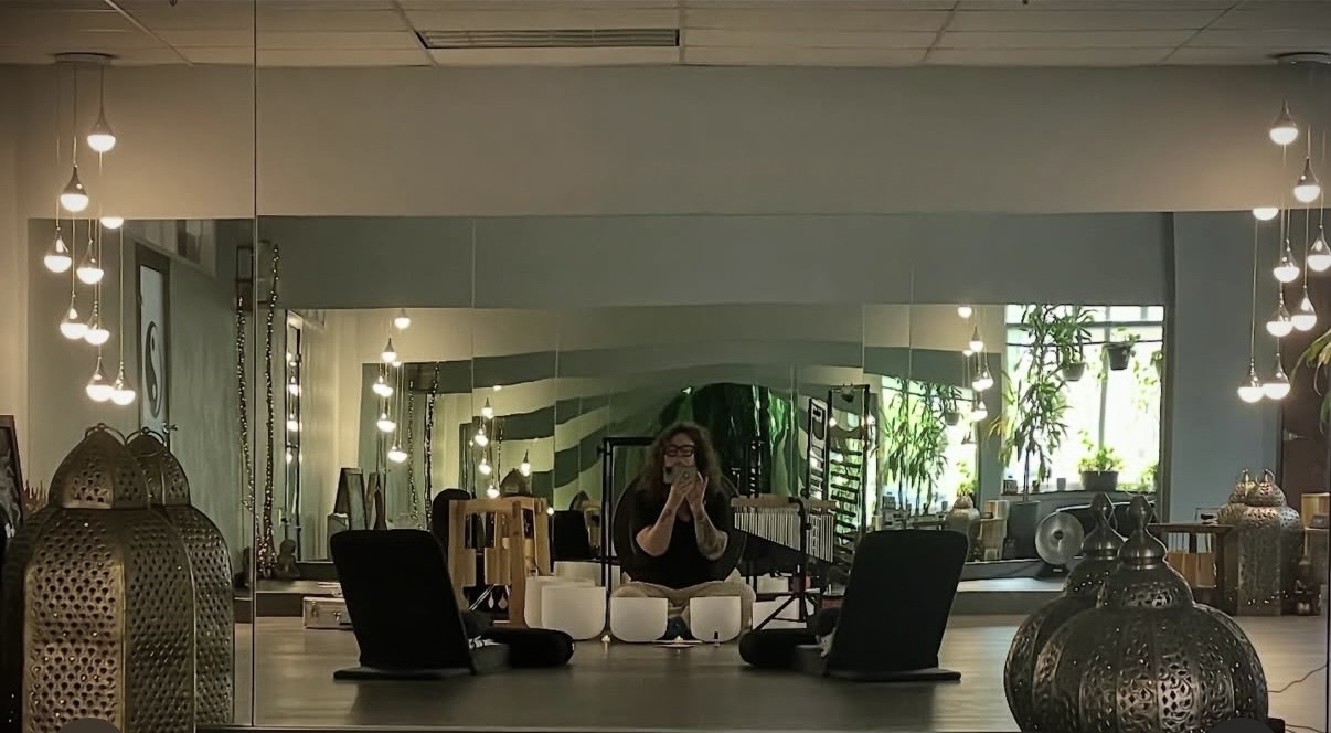 Person taking a photo in front of a large mirror with decorative objects and plants in the background.