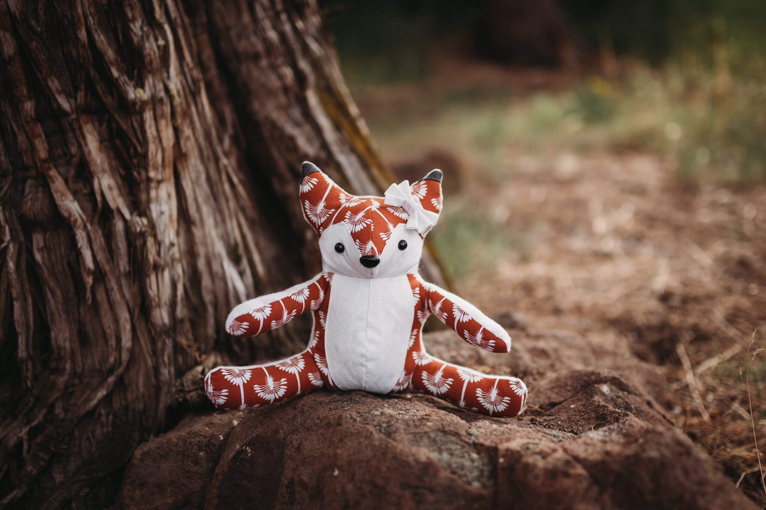 Plush tiger toy sitting on a rock near a tree trunk outdoors, with blurred natural background