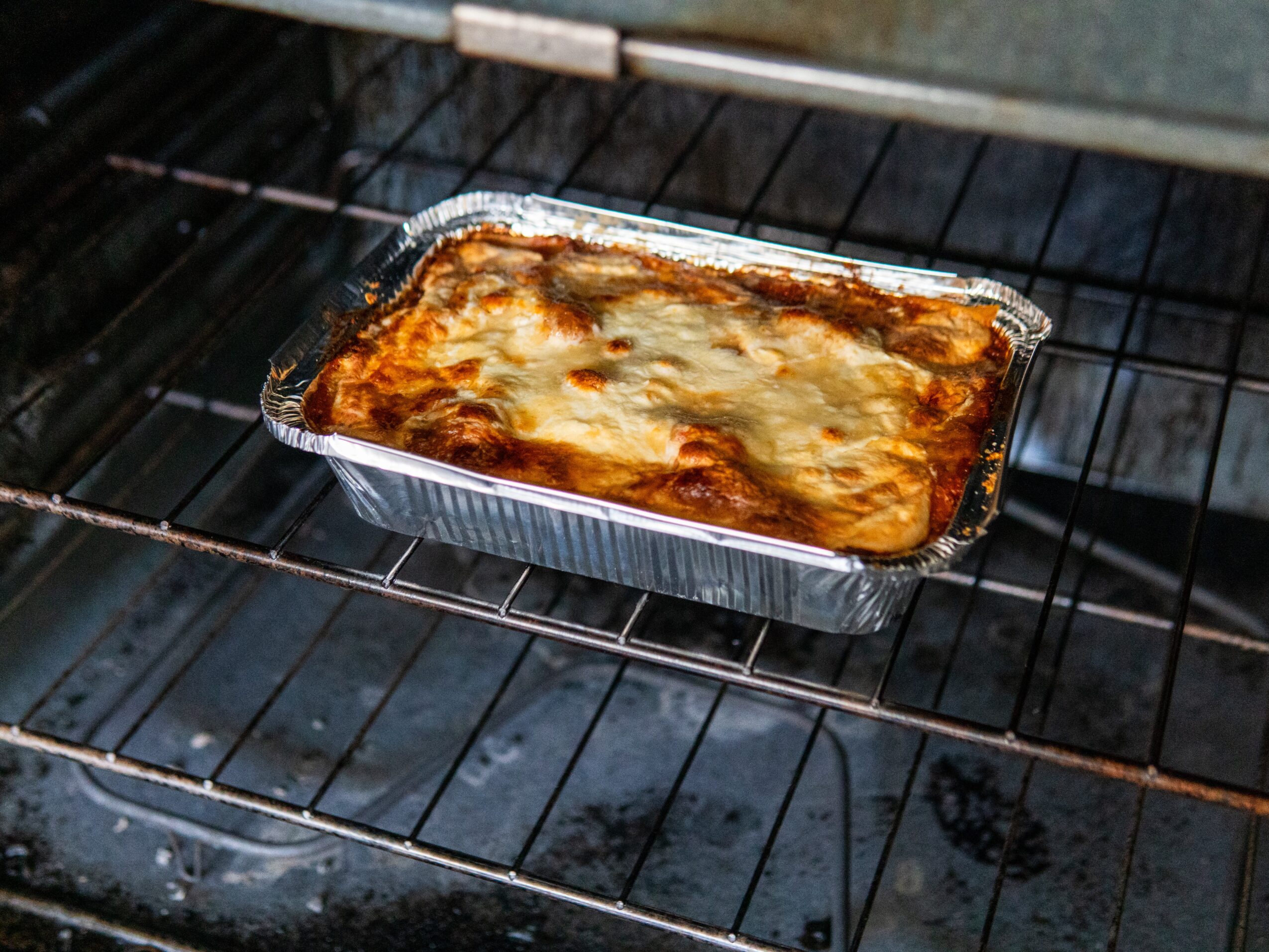 Lasagna baking in an aluminum tray inside an oven, with melted cheese on top.