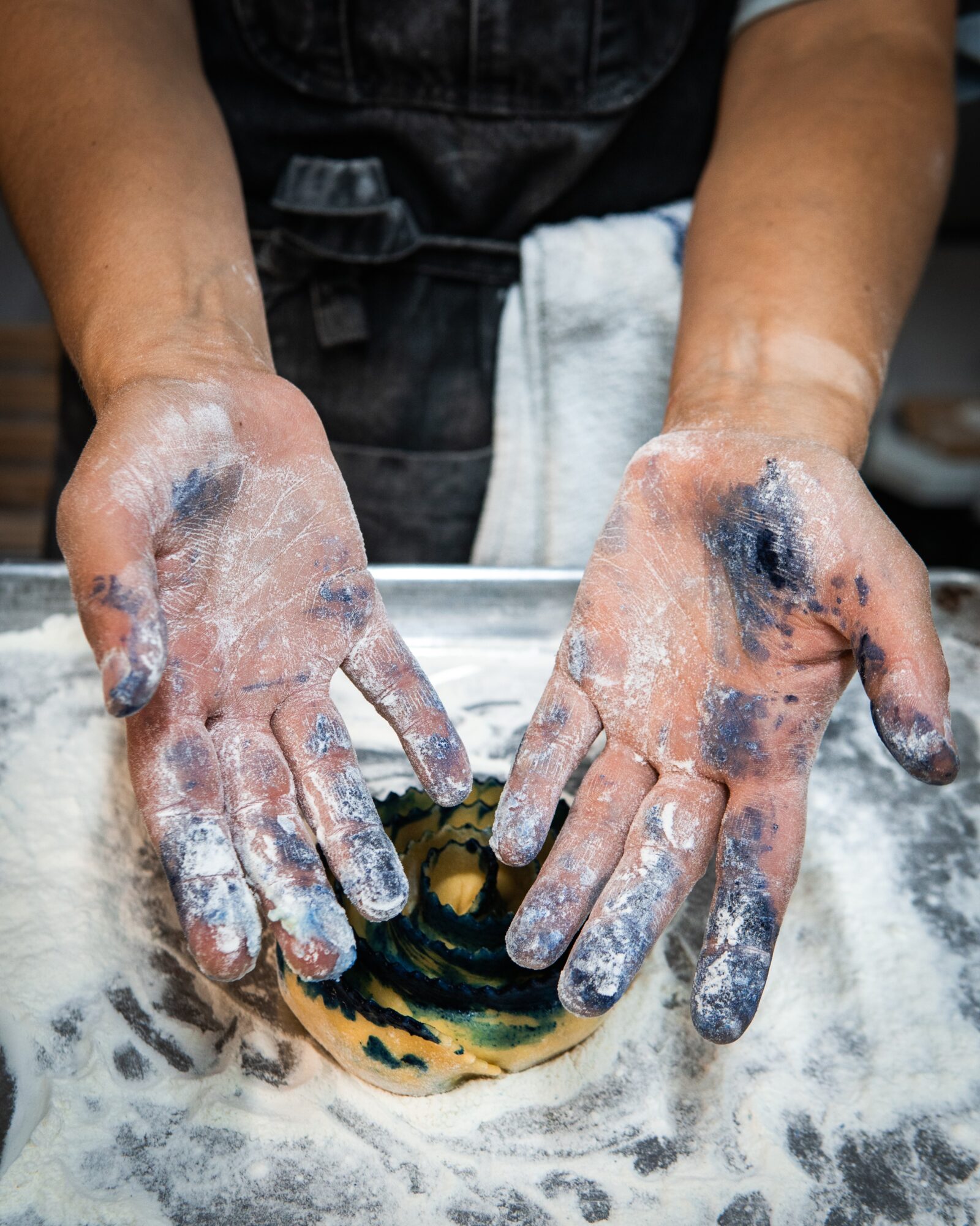 Person's hands covered in flour, shaping dough on a floured surface, with a towel around their waist.
