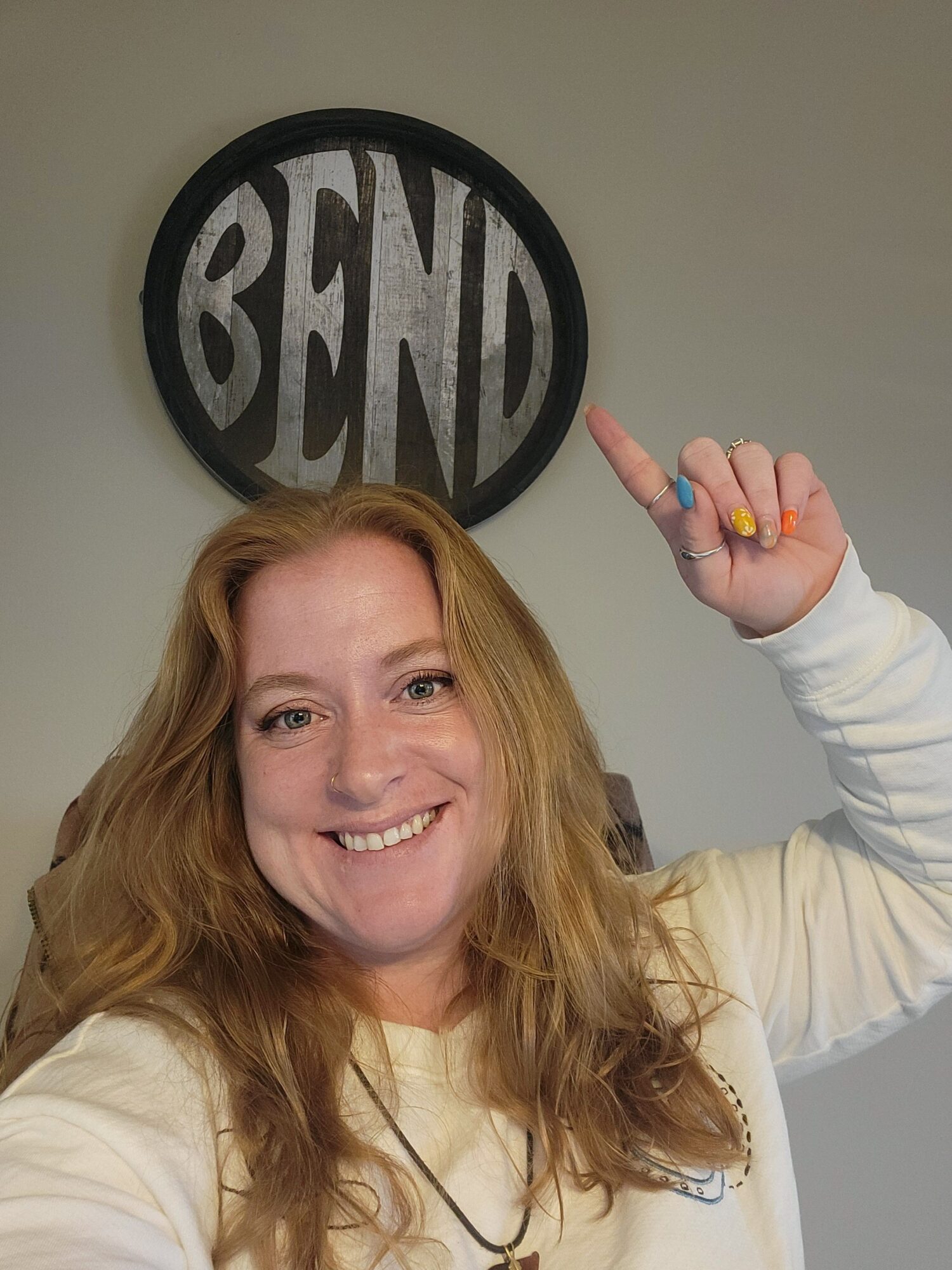 Woman with long hair smiling and pointing at a round sign on the wall.