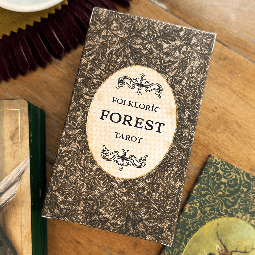 Tarot card deck titled 'Folkoric Forest Tarot' with a leafy pattern background, placed on a wooden surface.