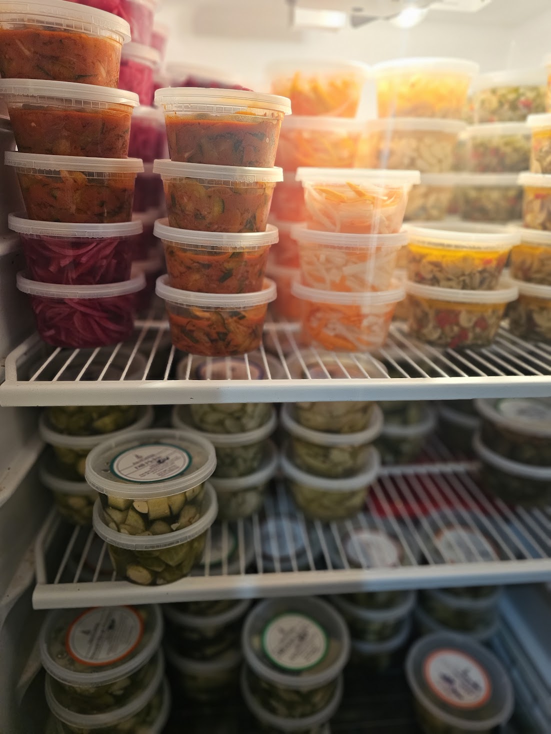 Stacked containers of prepared food on refrigerator shelves, with various colors and types of dishes visible.