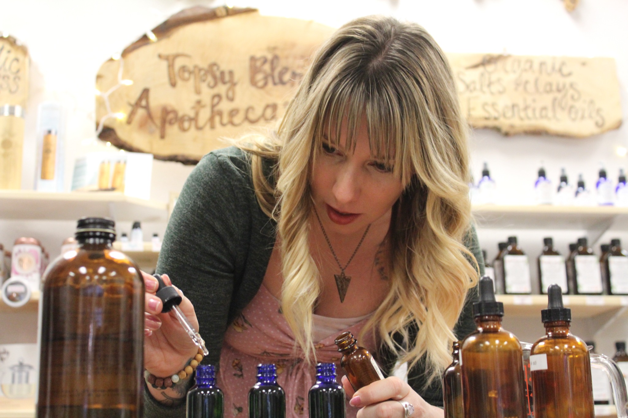Woman with blonde hair and bangs looking at bottles in a store, shelves with products in background