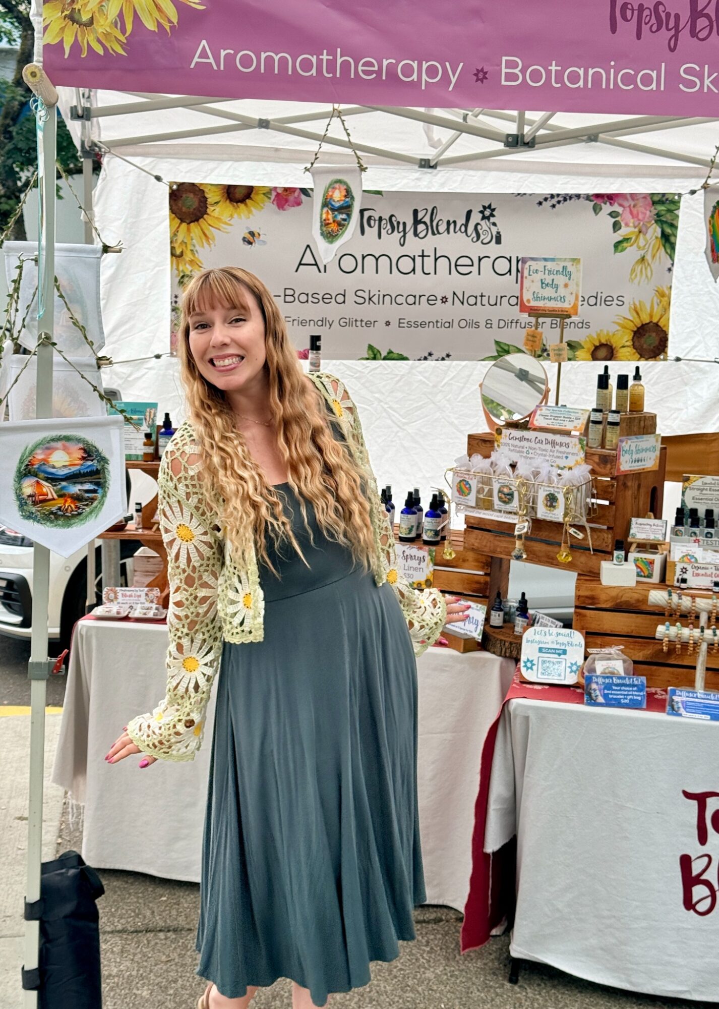 Young woman with long hair smiling at a booth selling skincare products at an outdoor market.