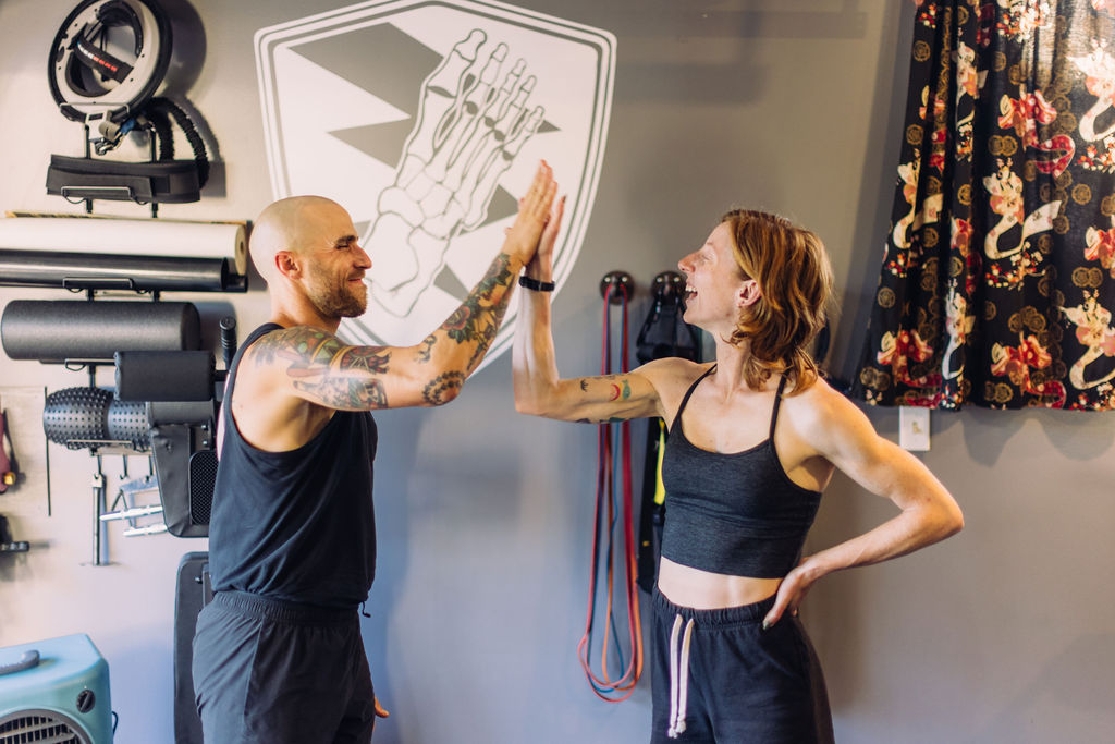 Two people high-fiving indoors, with fitness equipment and a colorful curtain in the background.