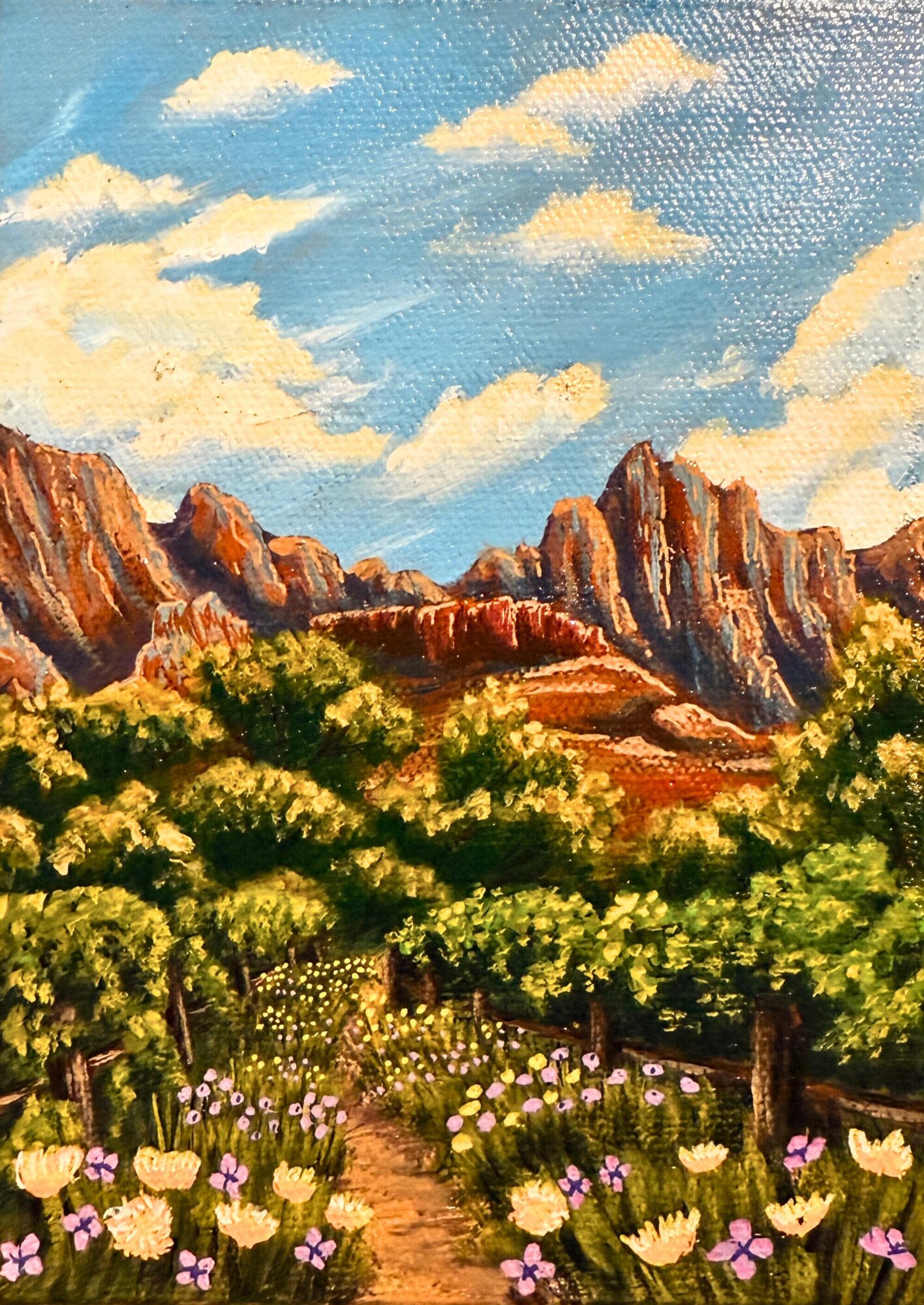 Landscape with mountains, green trees, and a flower garden under a partly cloudy sky.